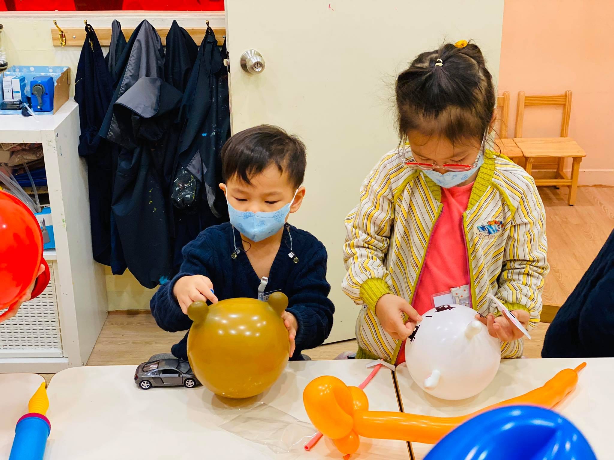 兩個孩子在桌上替咖啡色和白色圓氣球畫上眼睛與表情