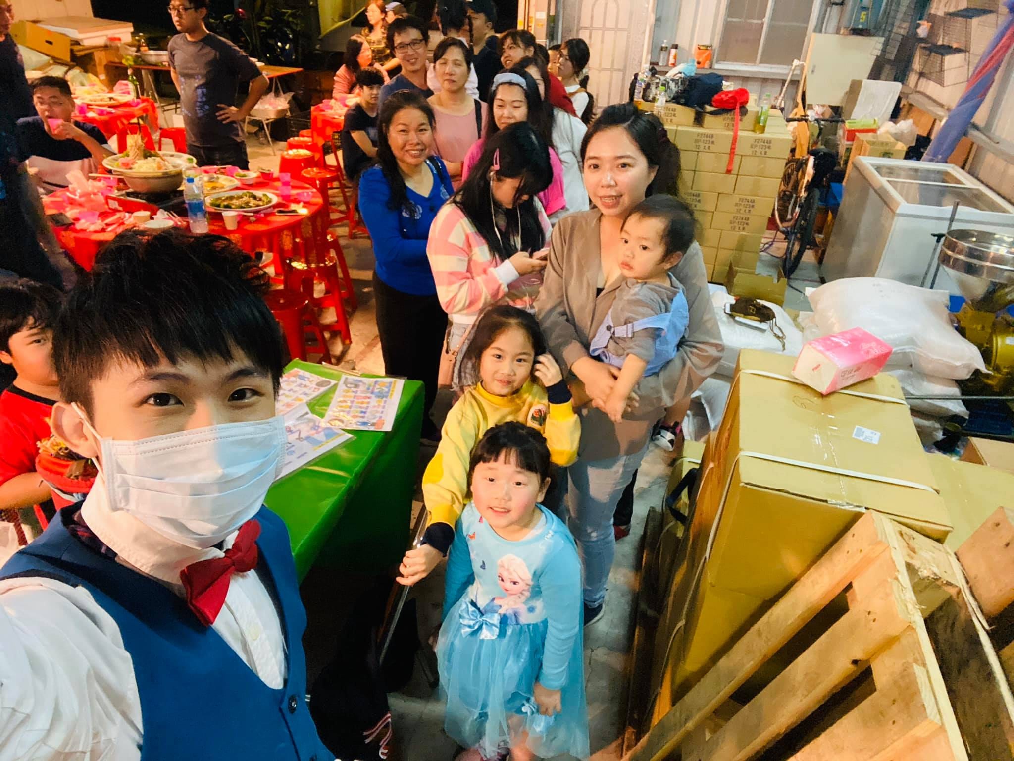 公司春酒辦桌旁，我戴口罩自拍，身後排著等氣球的家長與小朋友
