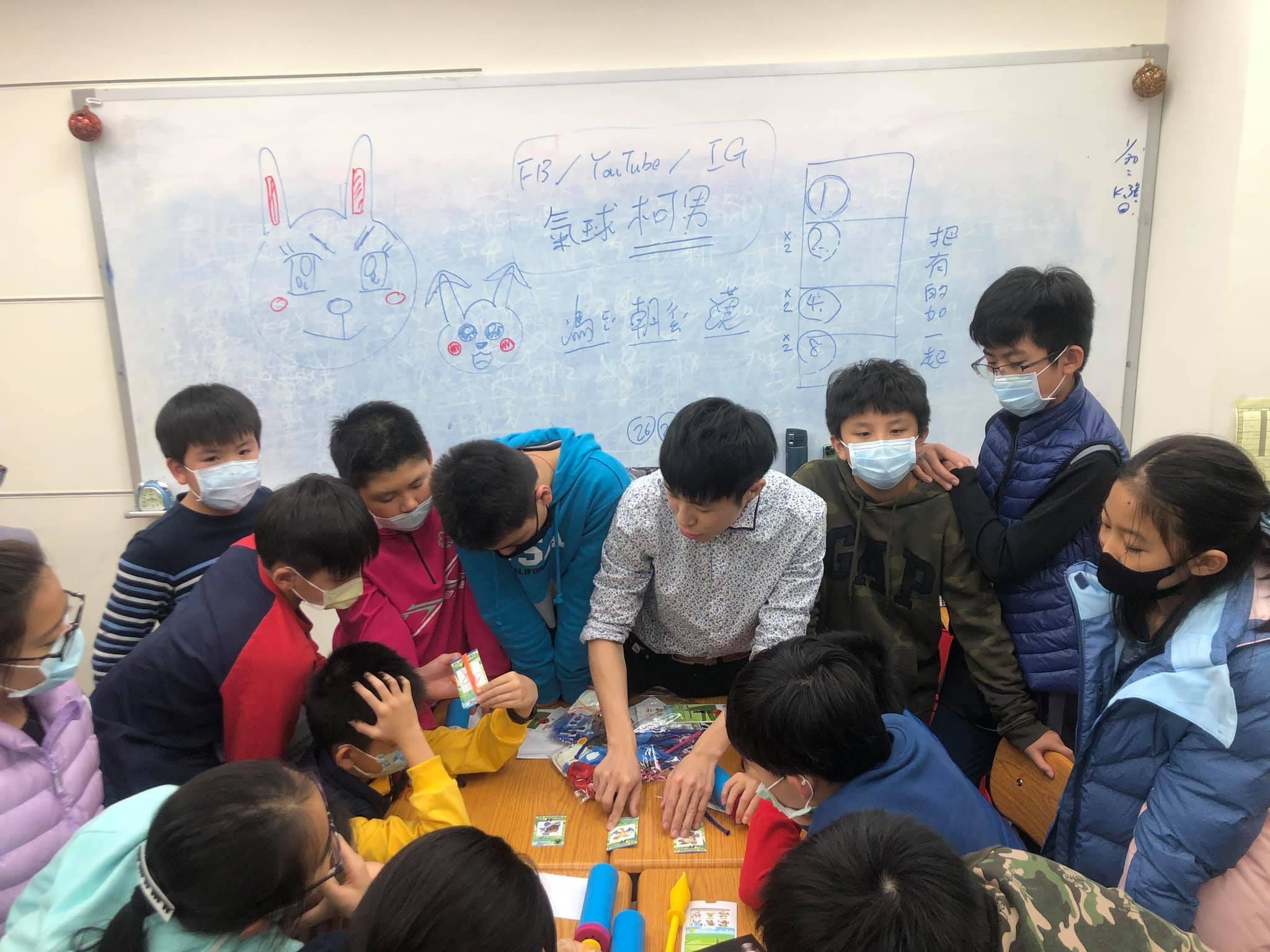 白板前一群學生圍在桌邊,低頭看桌上的魔術道具
