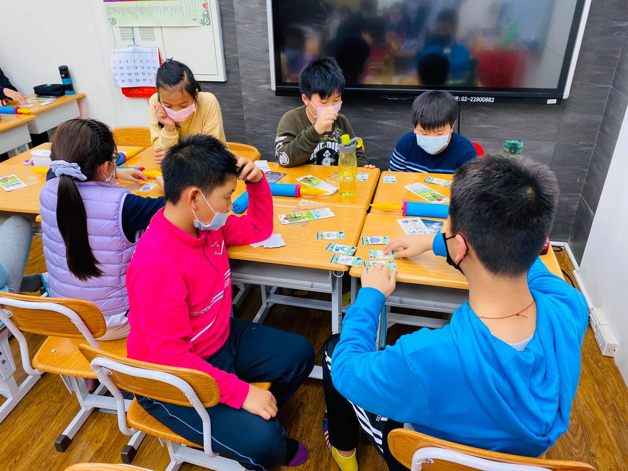 穿桃紅色與藍色外套的學生面對面,在課桌上練習魔術手法