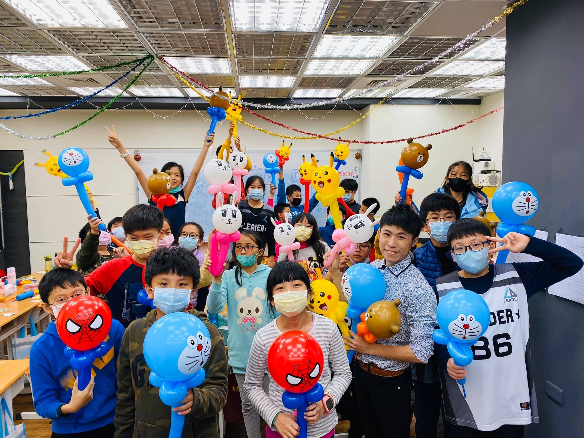 冬令營教室裡,戴口罩的學生舉著蜘蛛人、哆啦A夢與小熊造型氣球合照