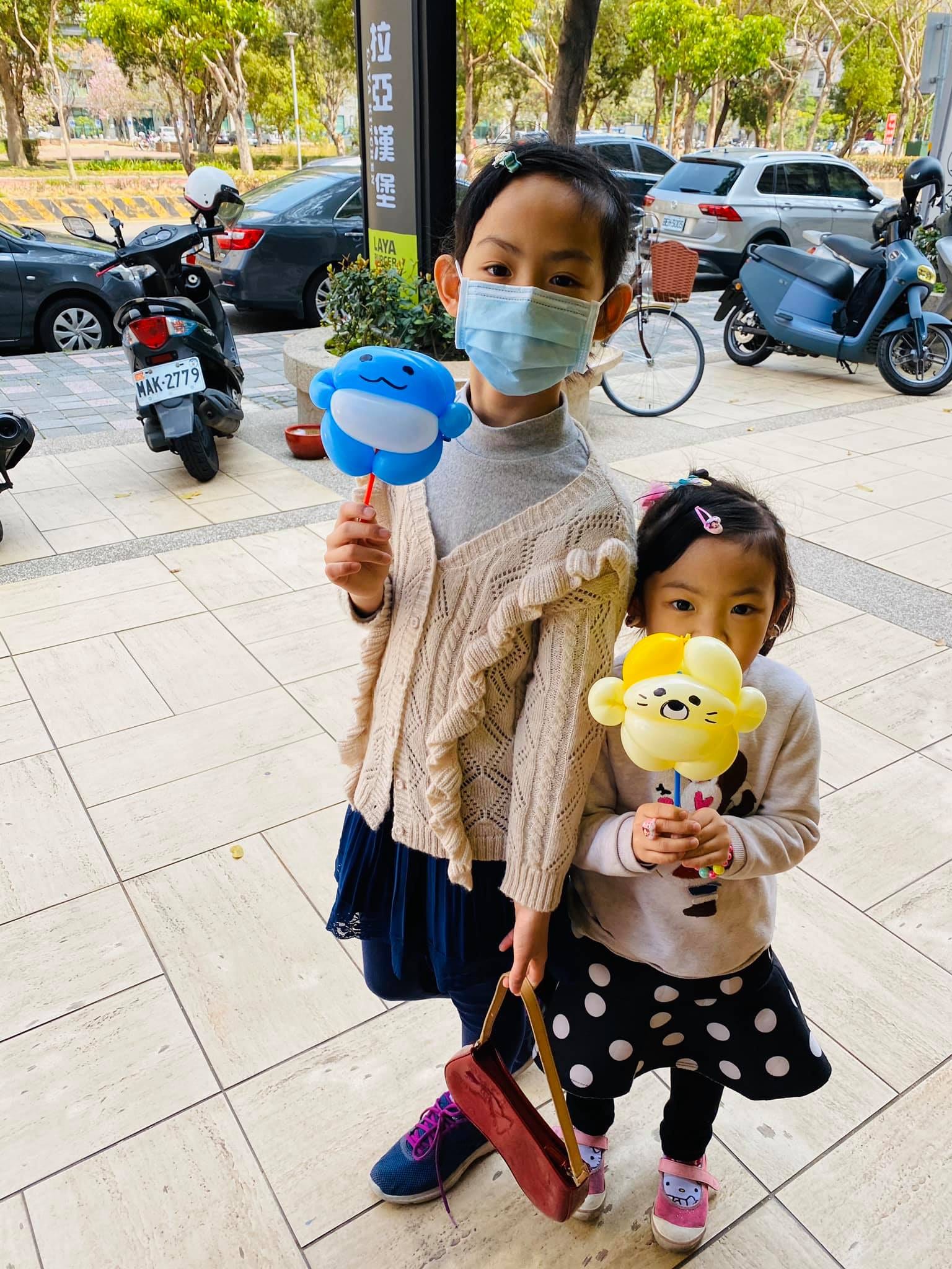 姊妹倆在拉亞漢堡招牌前，拿著巧虎和藍色圓臉造型手拿棒