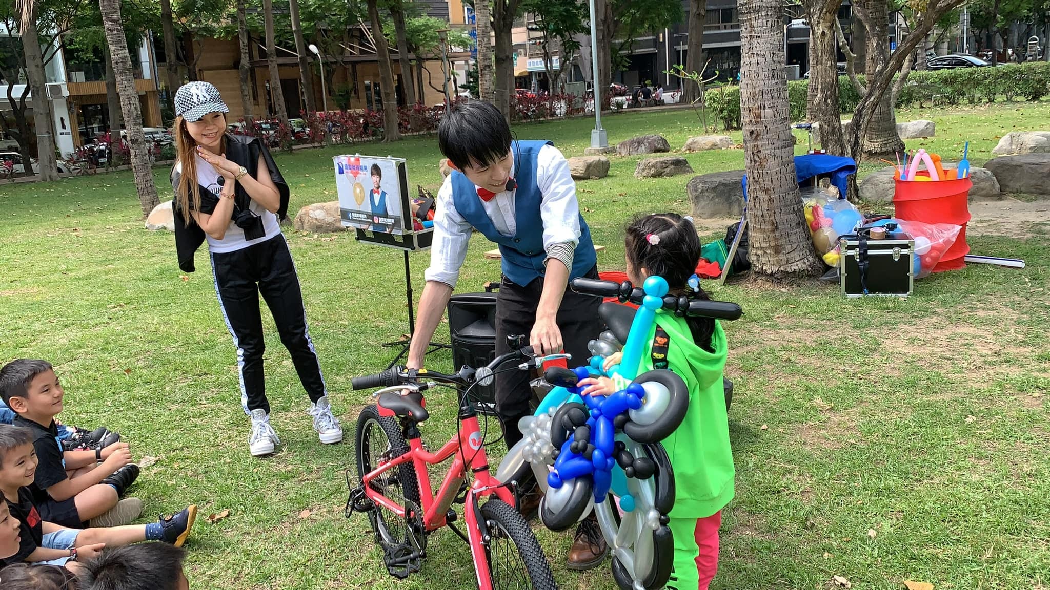 紅色真實腳踏車旁,小壽星抱著藍白腳踏車造型氣球