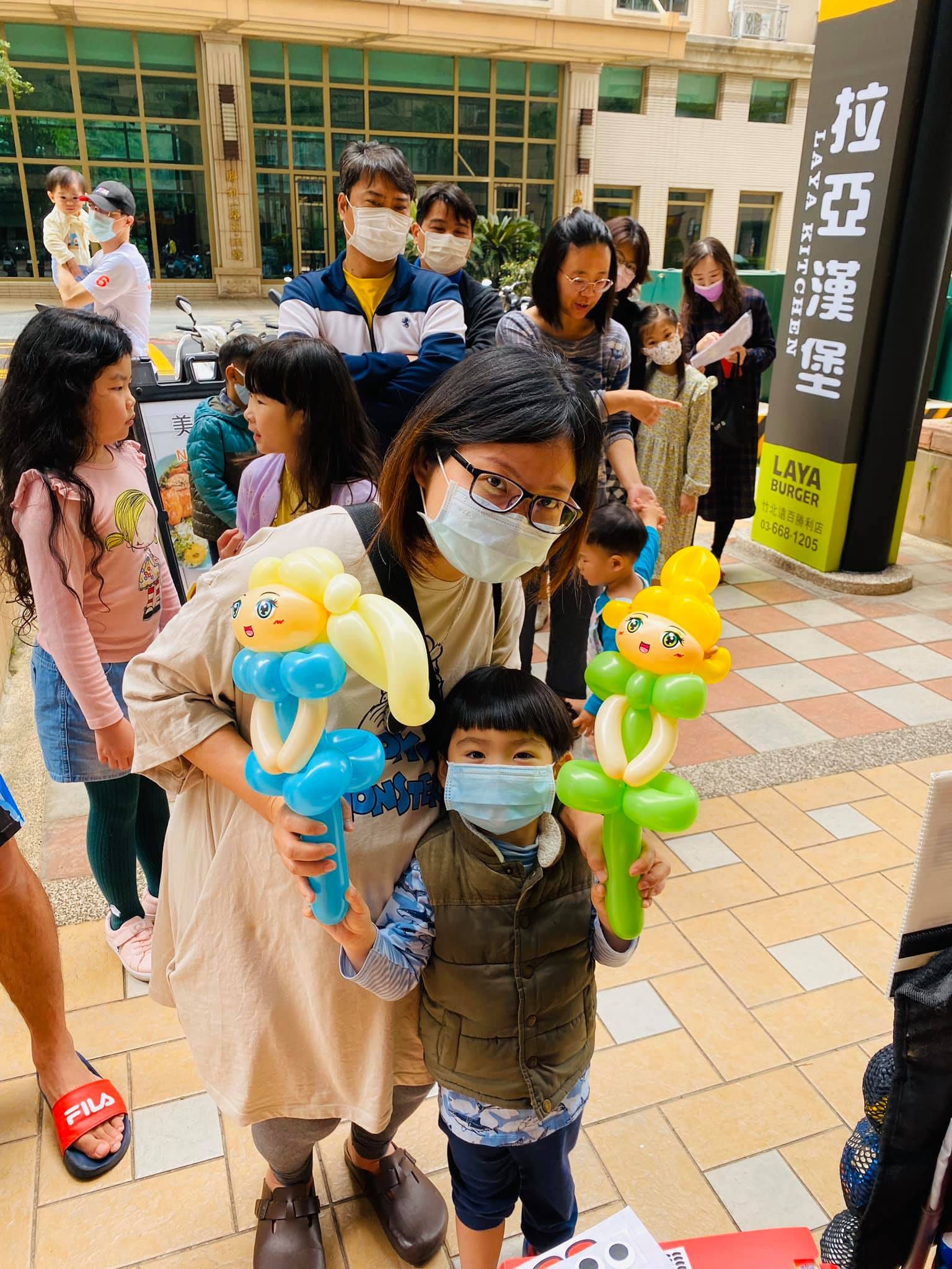 媽媽和兒子各拿一支金髮娃娃造型氣球，藍色與綠色衣服