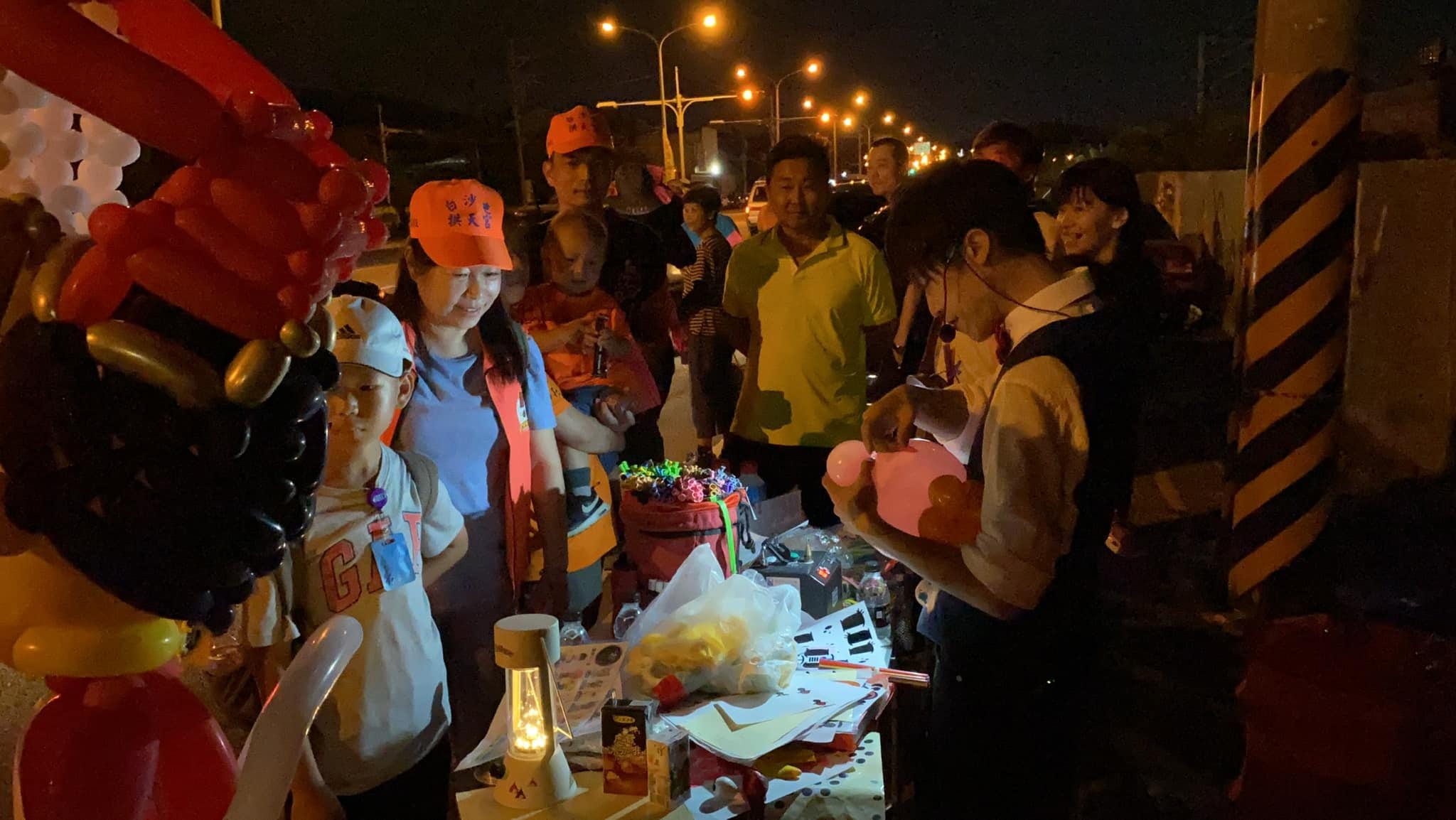 夜晚路邊攤位，戴拱天宮橘帽的信眾看我折氣球