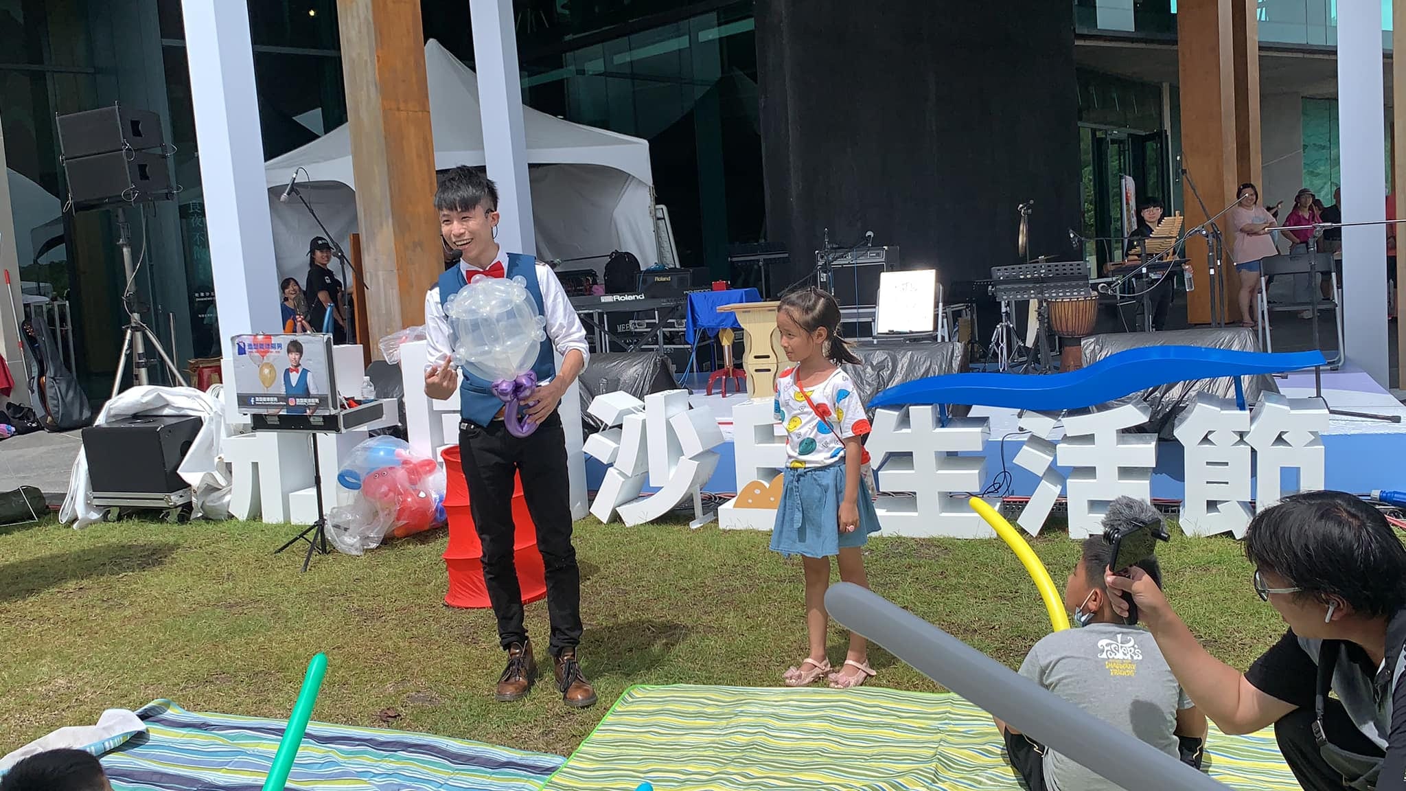 魔術師捧著透明紫色氣球花，笑著送給台上的小女孩