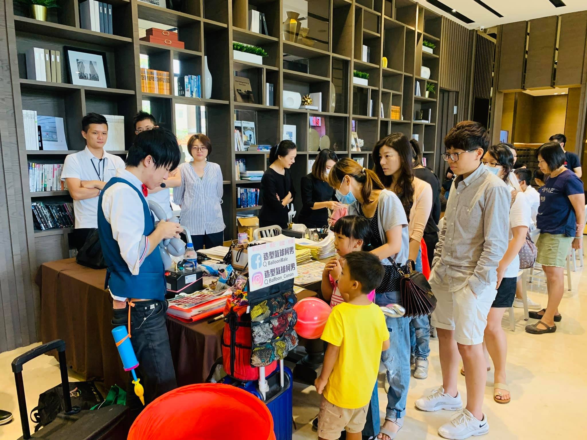 柯男在書櫃前的折氣球桌邊作業，大人小孩排隊等候