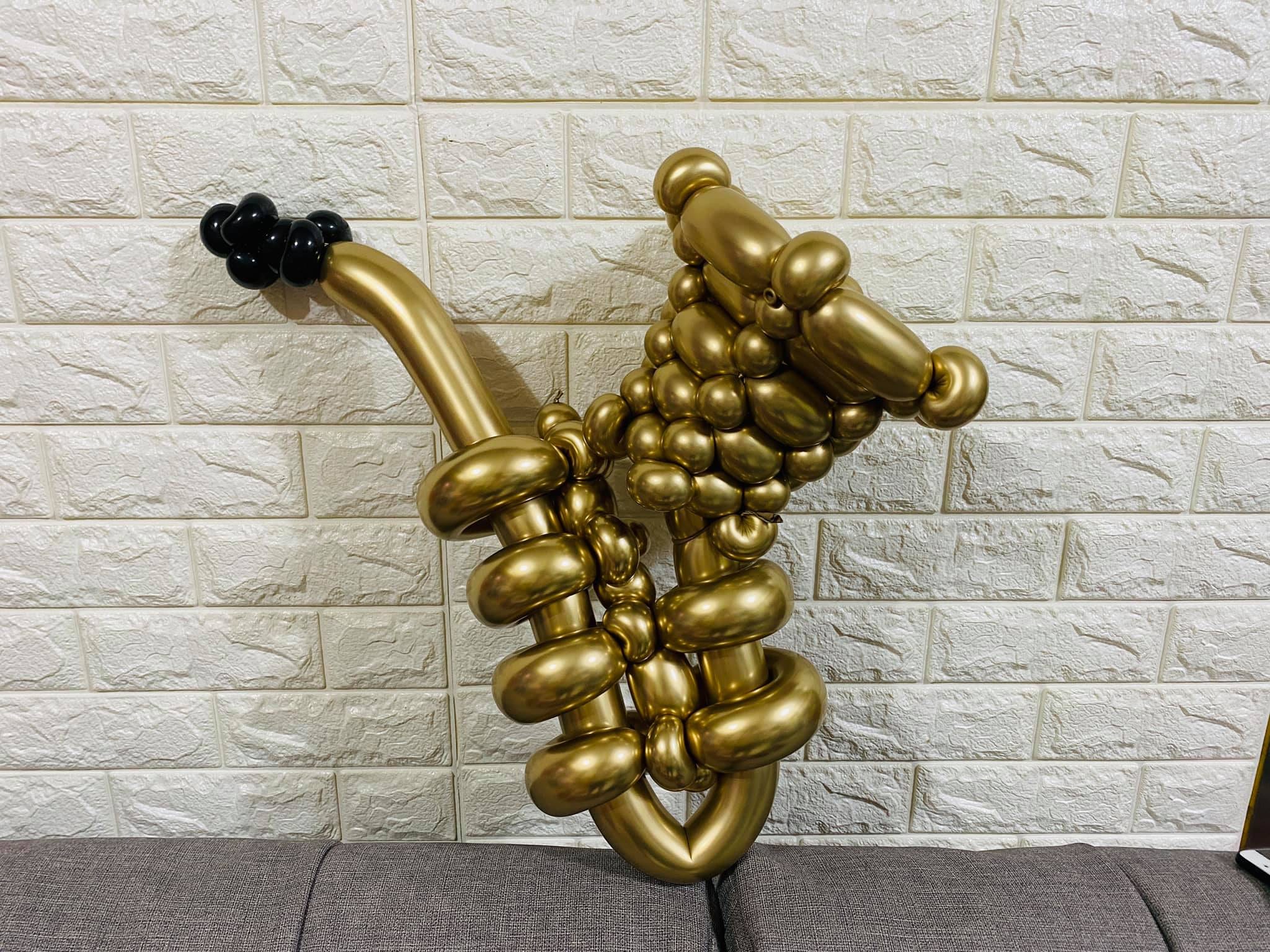 金色長條氣球編成的薩克斯風造型，黑色吹嘴靠在白磚牆前