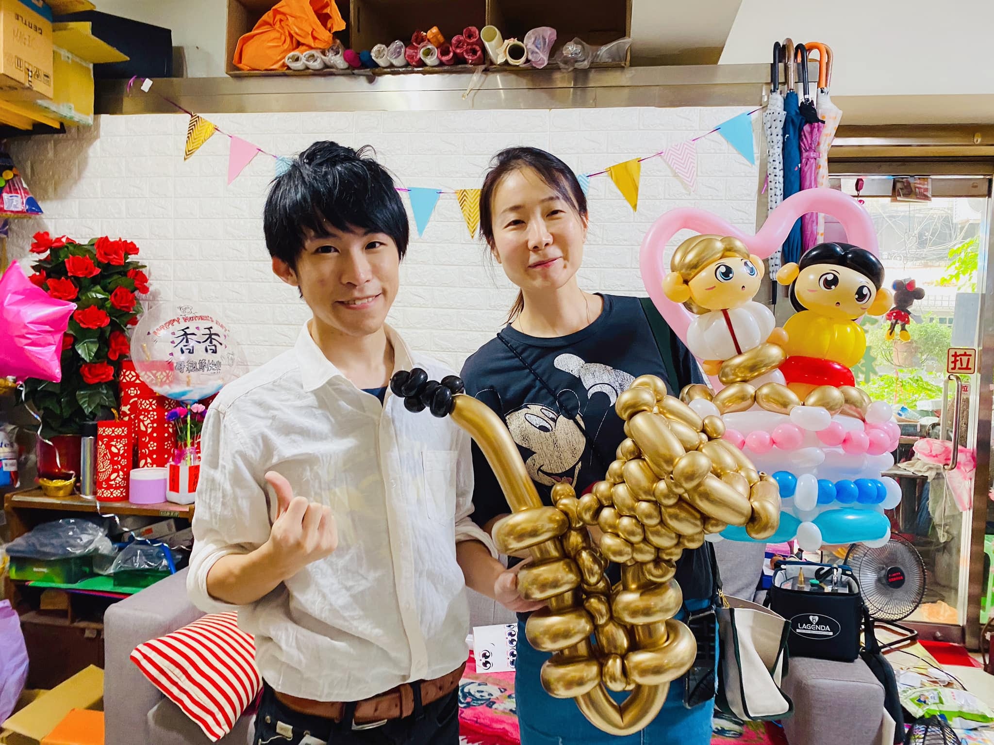 工作室裡兩人合照，手上拿著薩克斯風氣球與父子氣球蛋糕