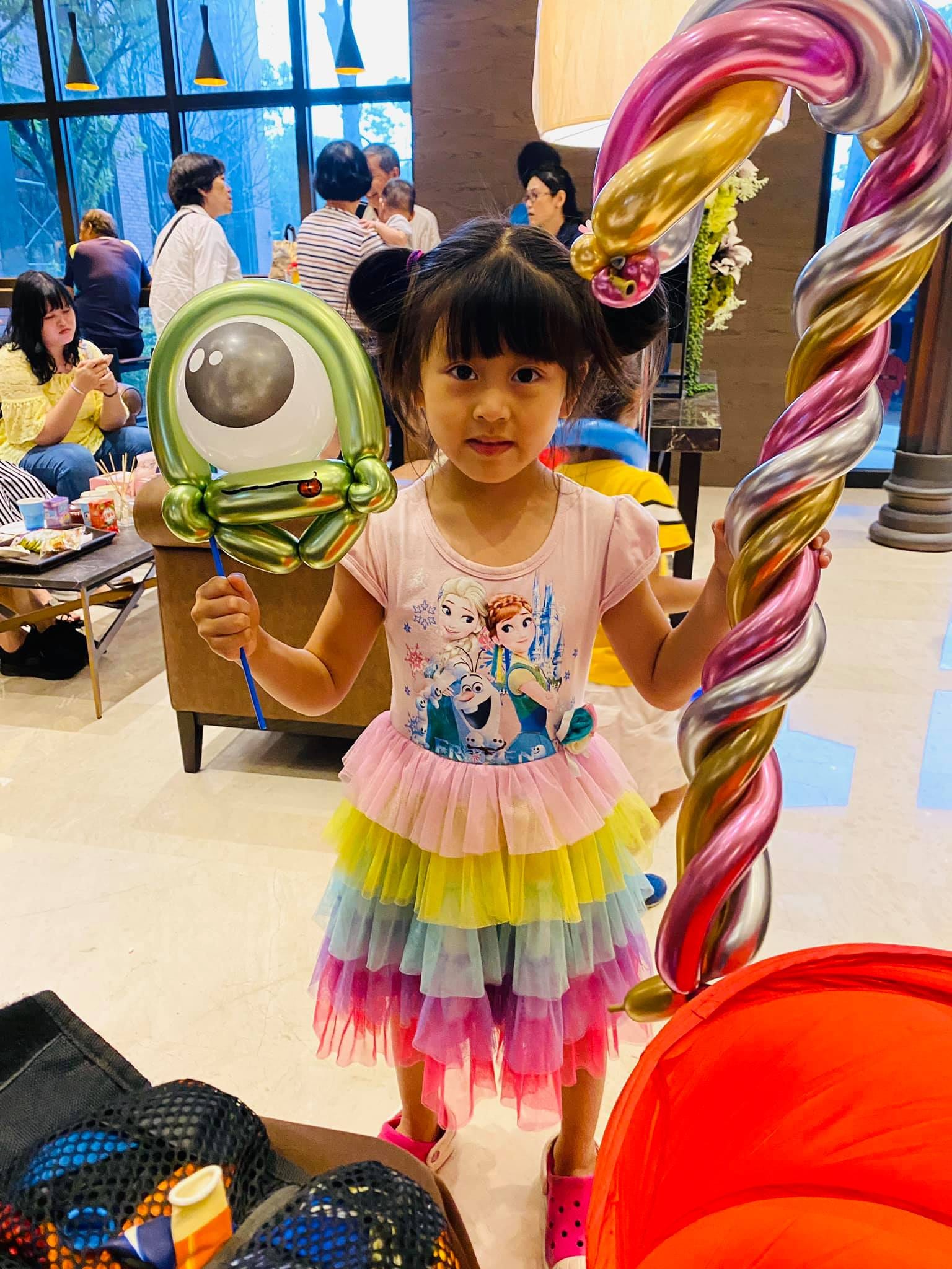 小女孩拿著綠色大眼怪與彩色金屬螺旋權杖氣球