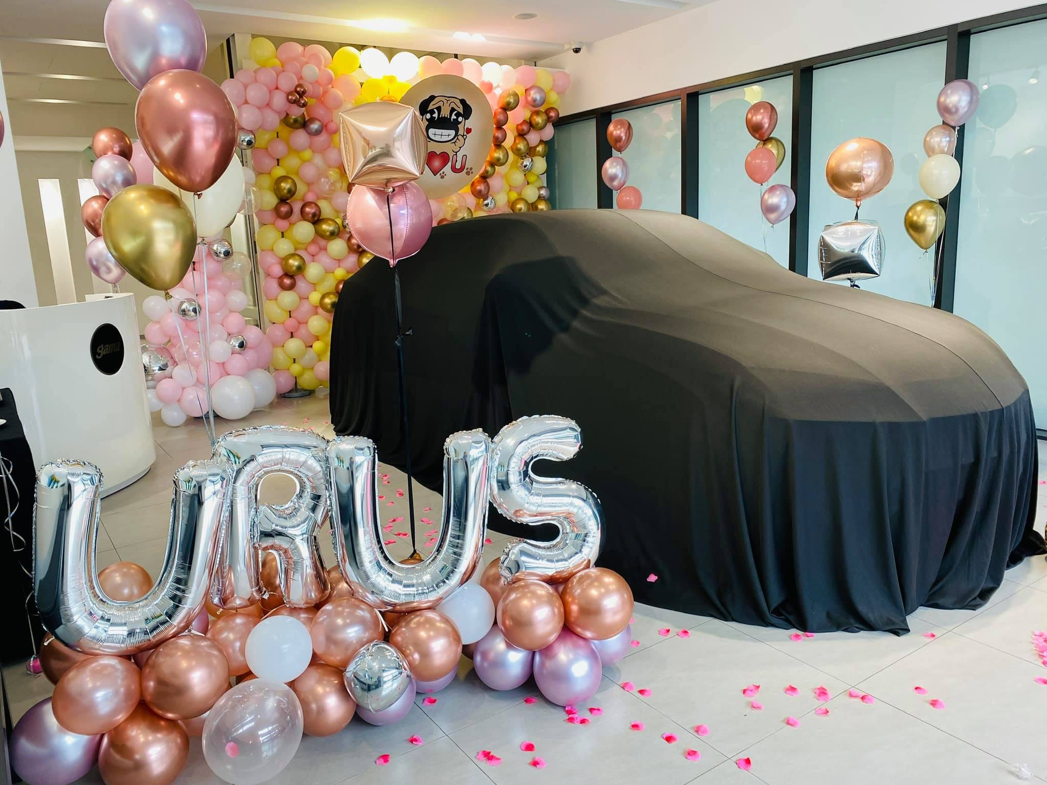 蓋著黑色車罩的新車旁，銀色 URUS 字母氣球與玫瑰金底座