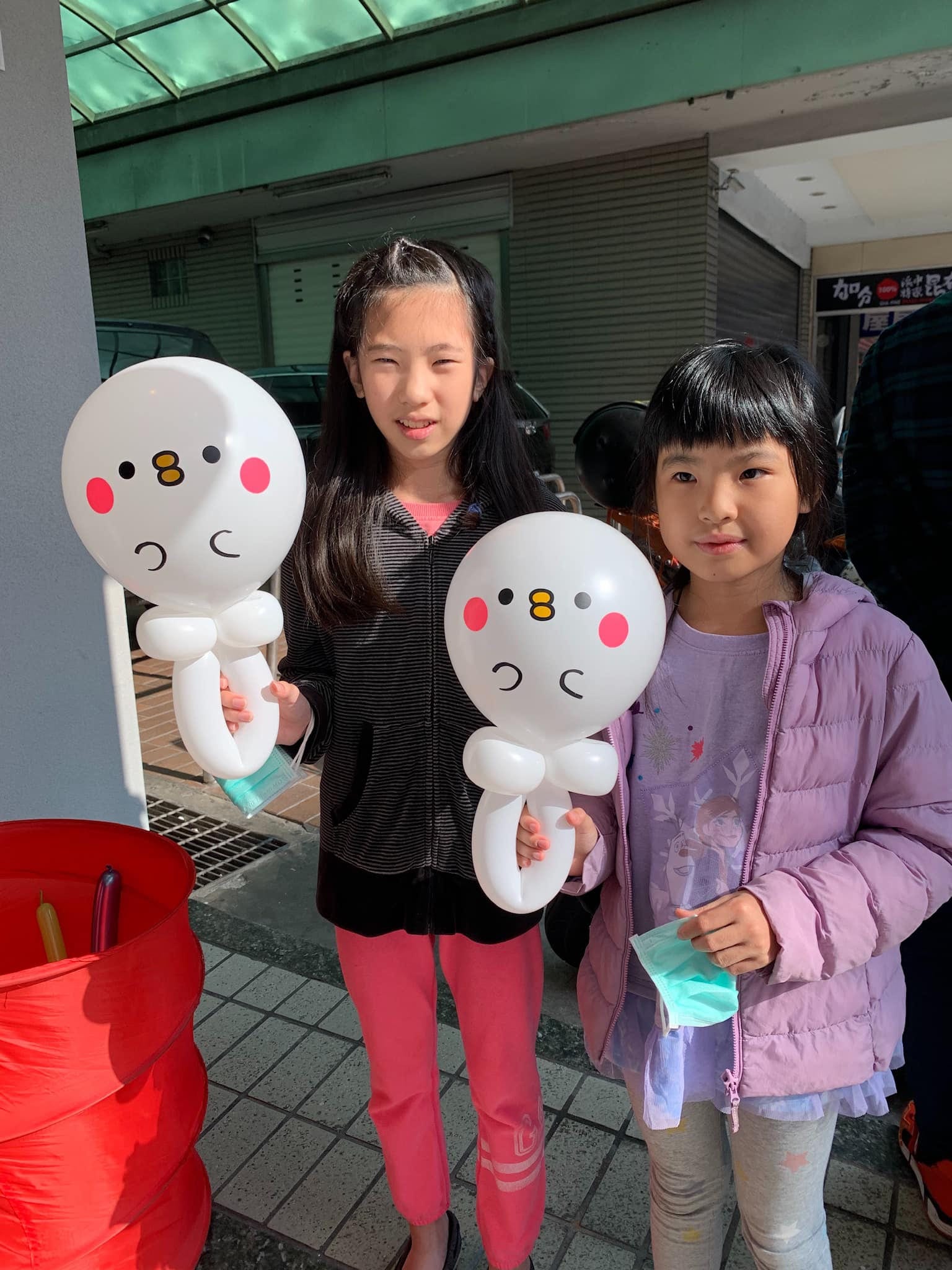 兩個小女孩各拿一支白色圓臉、粉紅腮紅的小鳥氣球