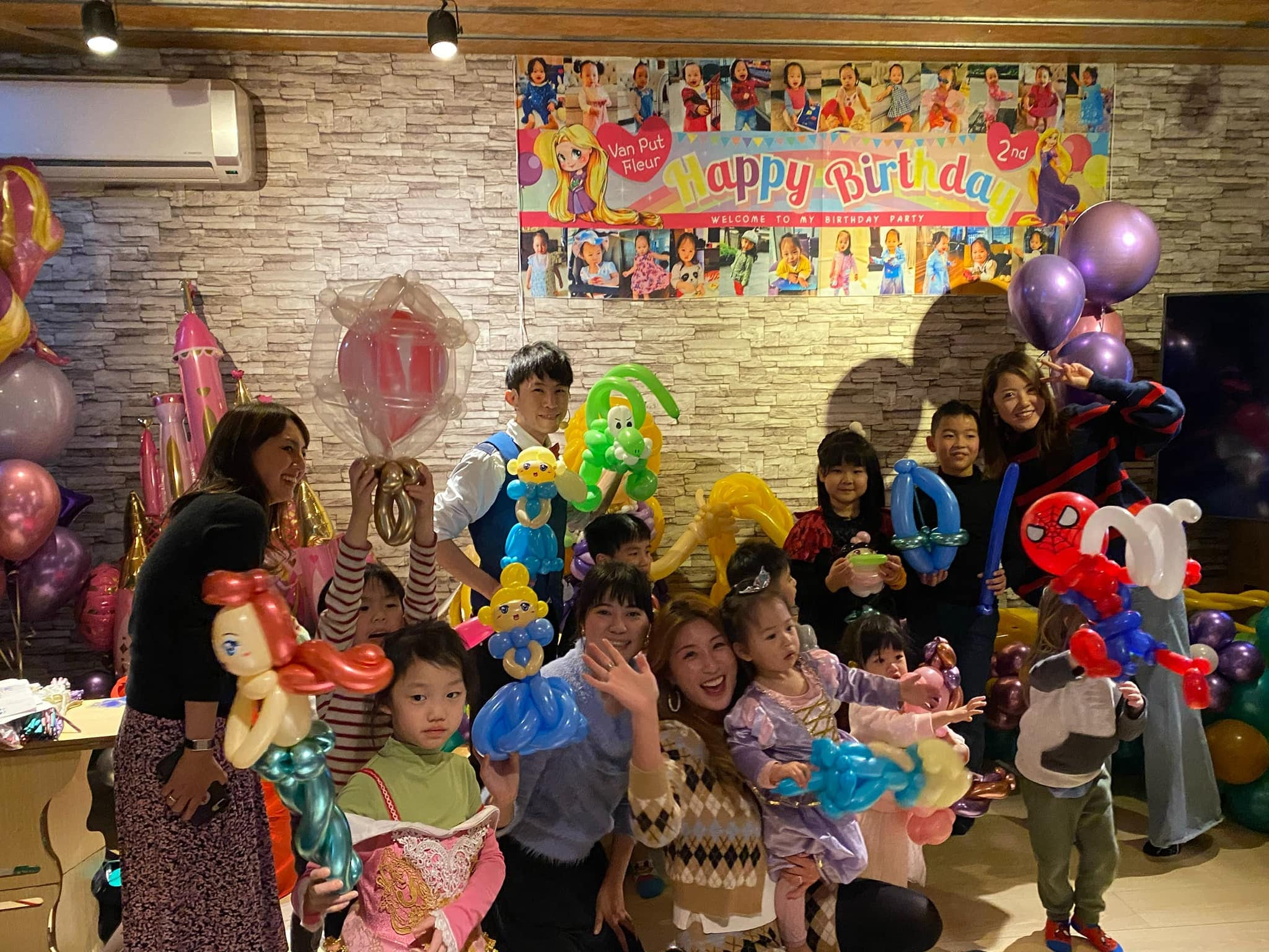 生日派對背板前大合照，大人小孩拿著小美人魚、蜘蛛人等氣球
