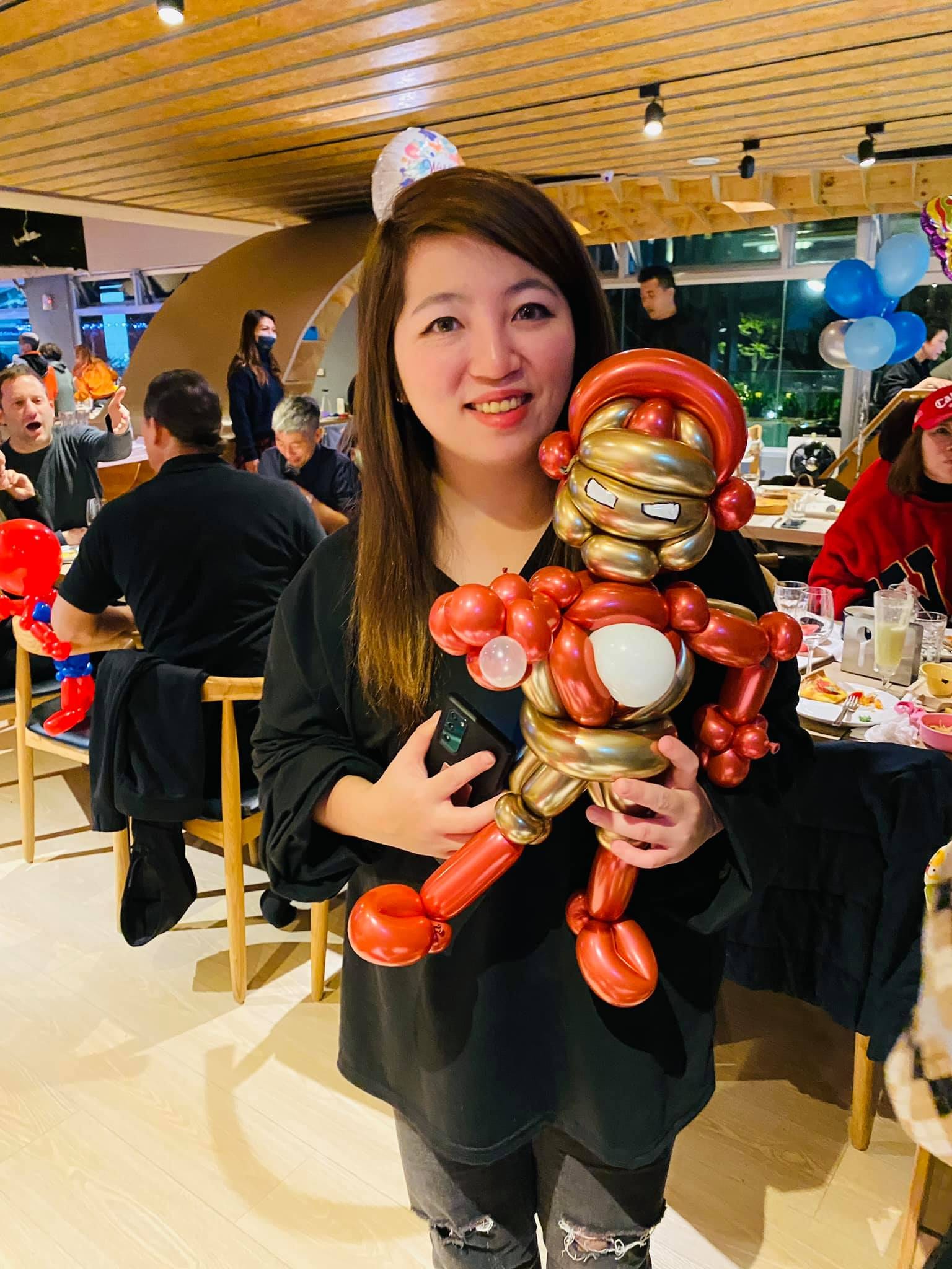 女士抱著紅金配色的鋼鐵人造型氣球站在餐廳