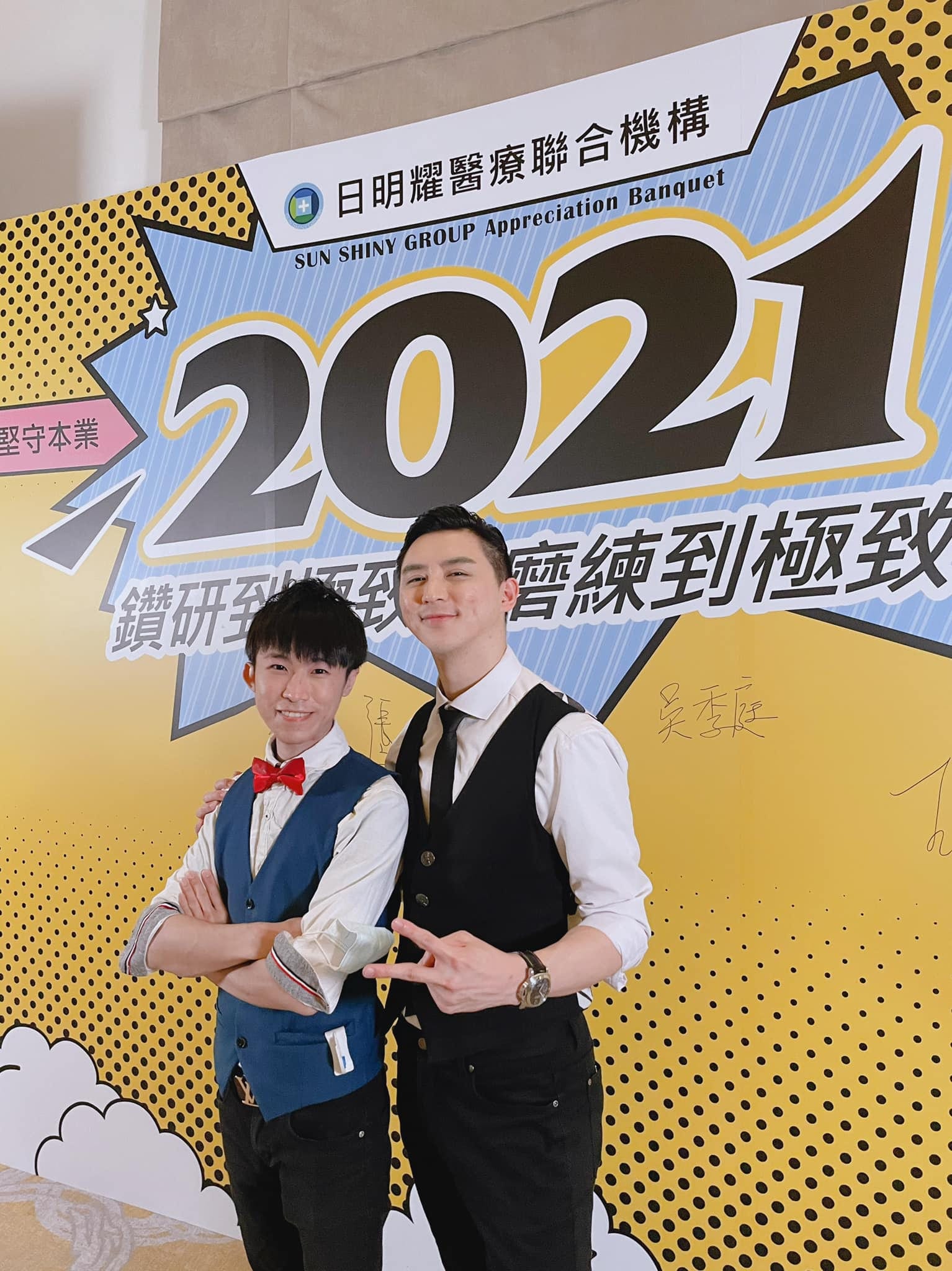 柯男與魔術師站在日明耀醫療聯合機構2021尾牙背板前合照