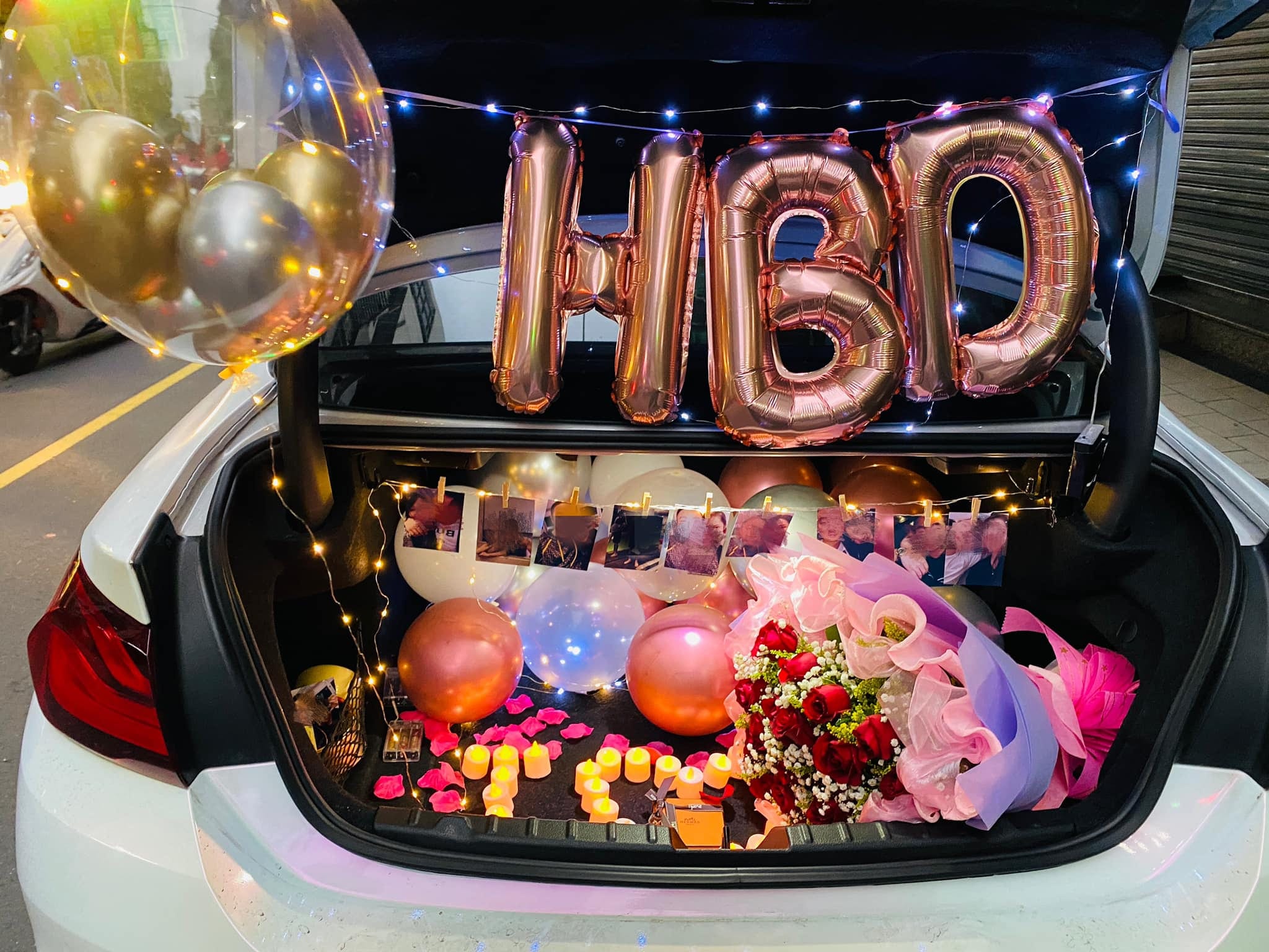 白色雙門轎跑後車廂生日佈置，玫瑰金HBD字母與照片串燈