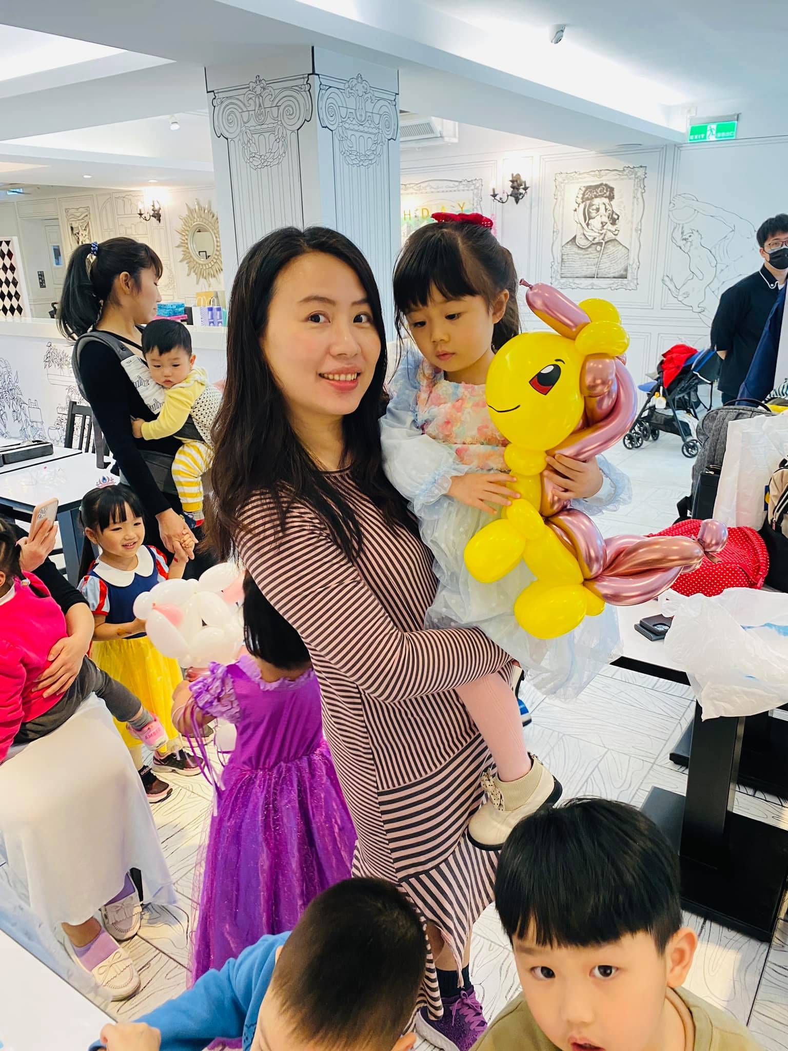 媽媽抱著女兒，女孩懷裡是粉紅鬃毛的黃色小馬氣球