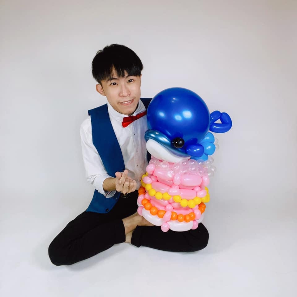 柯男坐在白色背景前，身旁是鯨魚蛋糕造型氣球