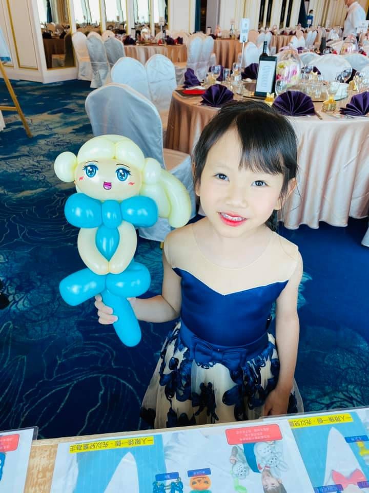 穿深藍洋裝的小女孩拿著艾莎造型氣球站在宴會廳