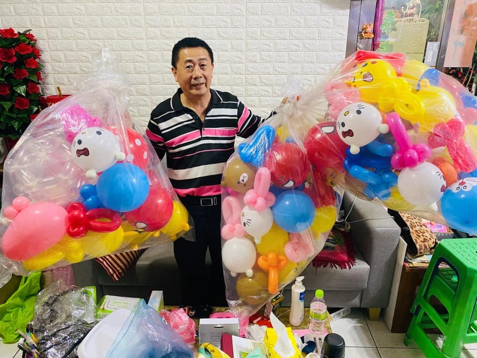 柯爹站在家中，兩旁是兩大袋預先折好的造型氣球