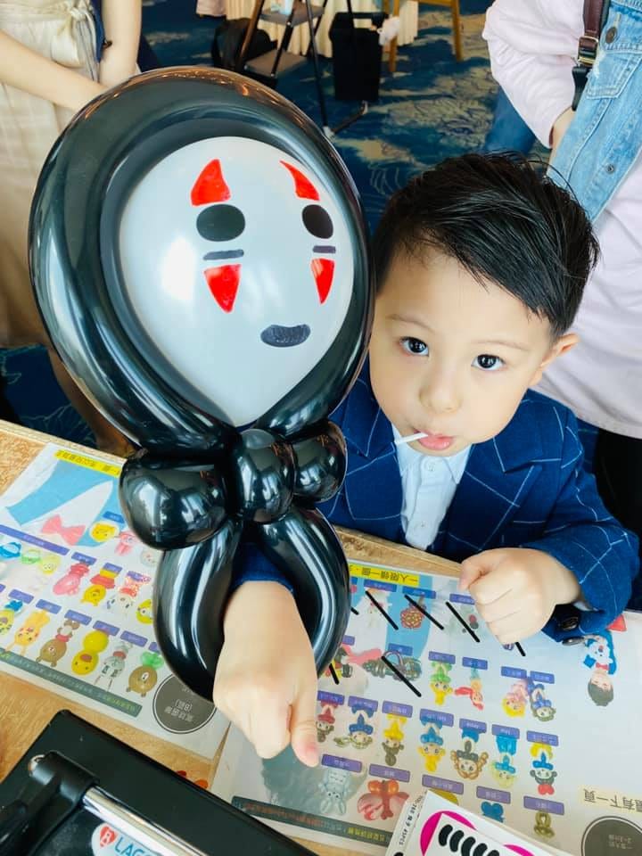 穿西裝的小男孩拿著無臉男氣球，桌上是造型選單