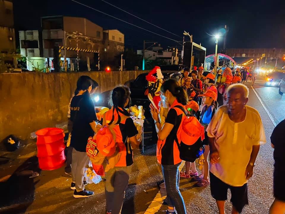 2020年夜晚馬路邊，戴紅帽的進香民眾排隊領氣球