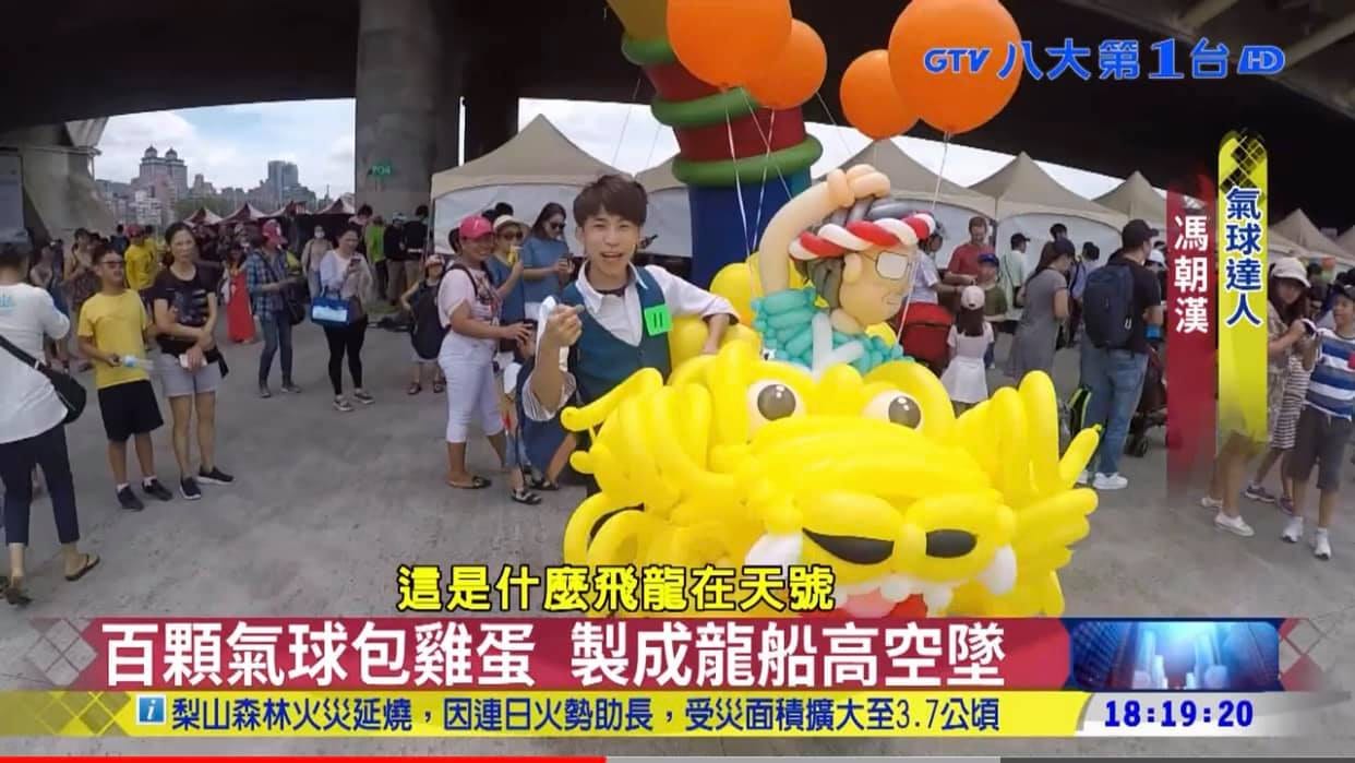 電視新聞畫面，柯男站在黃色金眼氣球龍頭後方受訪