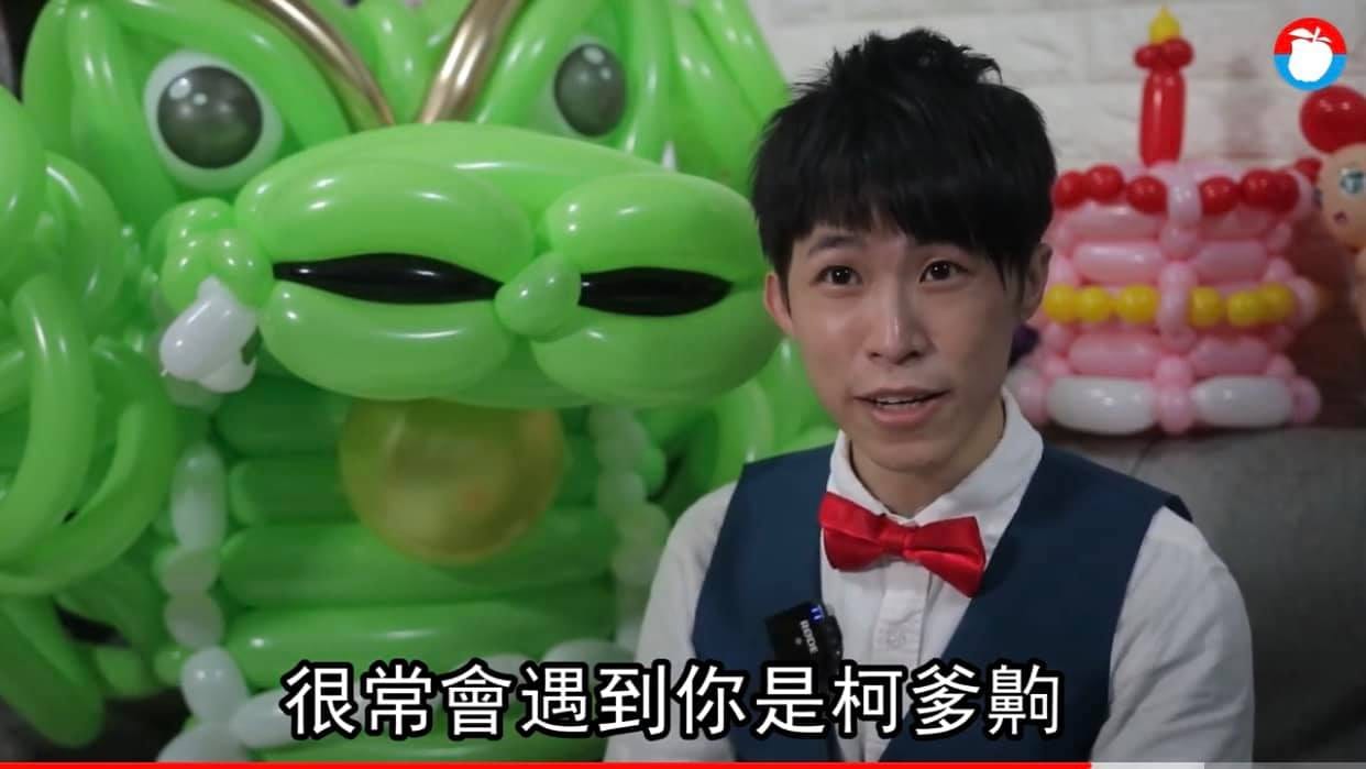專訪畫面，柯男坐在綠色氣球龍頭旁接受訪問