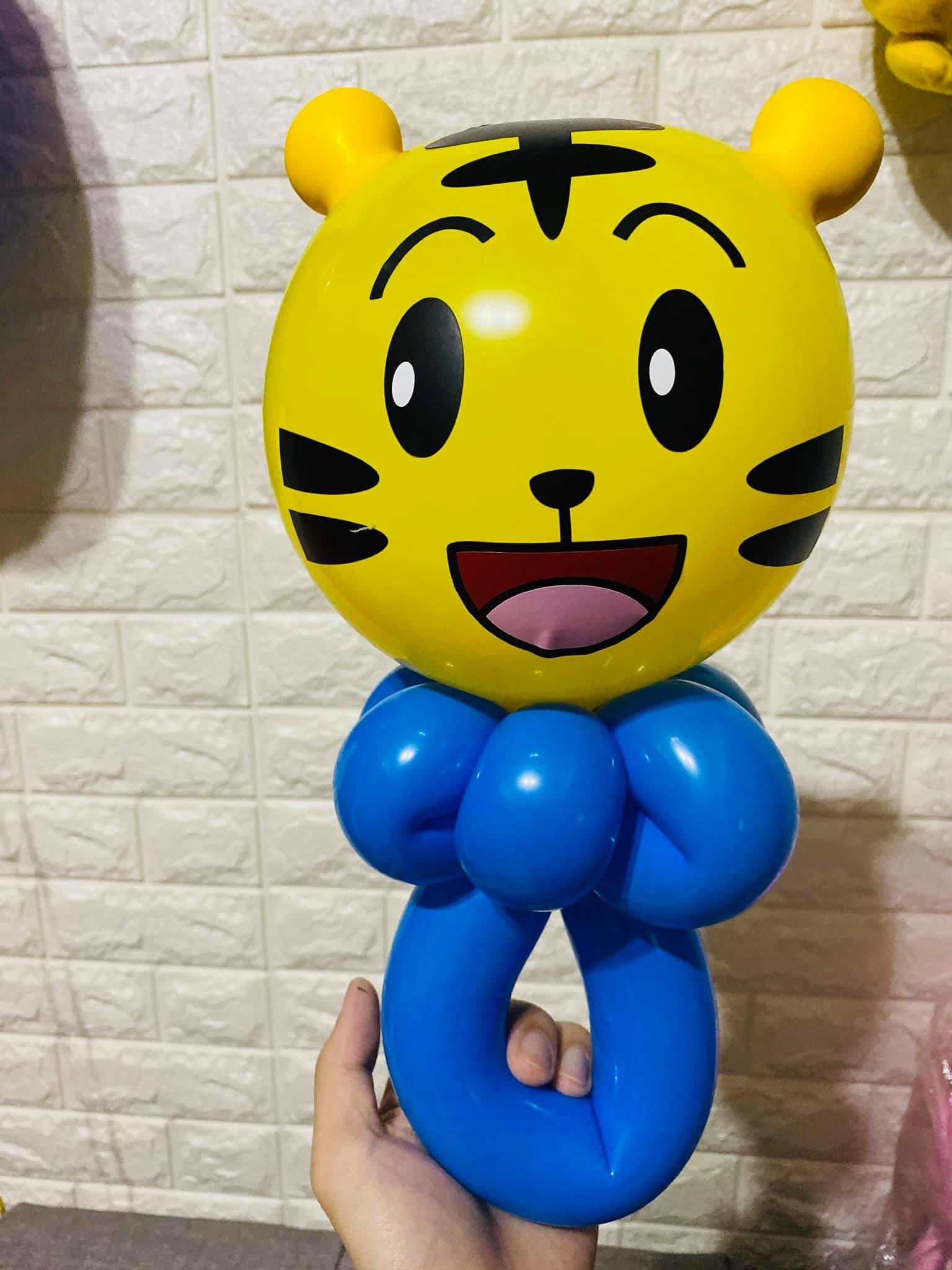 巧虎手持氣球，黃色圓臉加兩隻黃色耳朵，下面接藍色蝴蝶結與圓圈握把