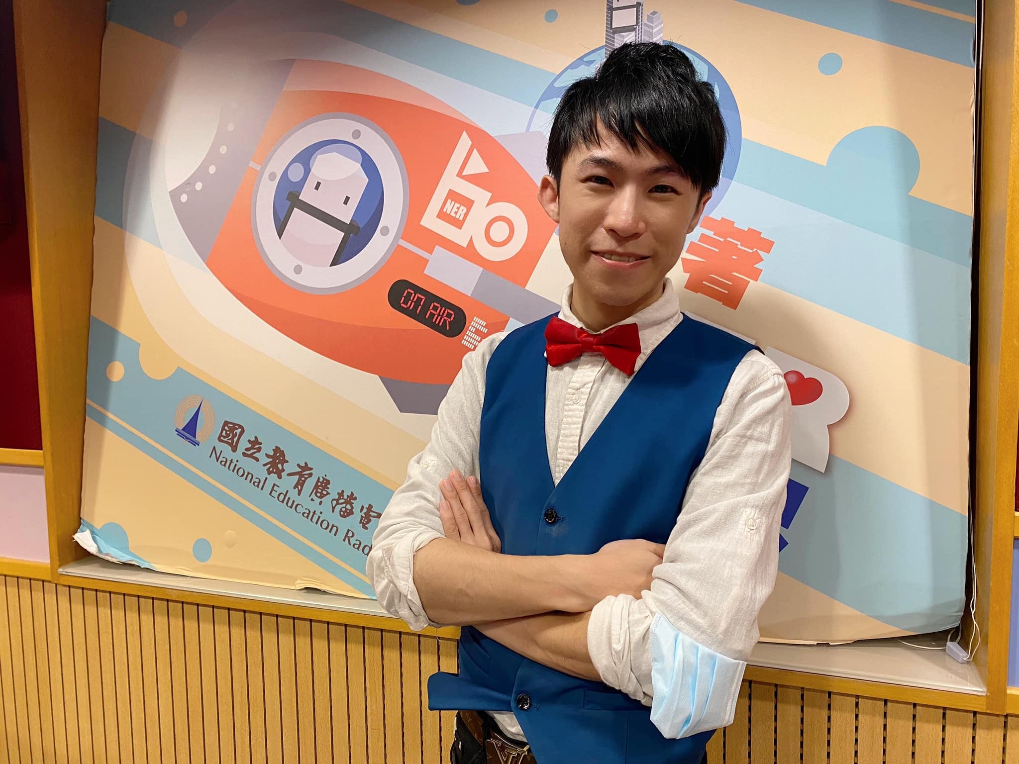 柯男雙手抱胸站在國立教育廣播電台的節目背板前