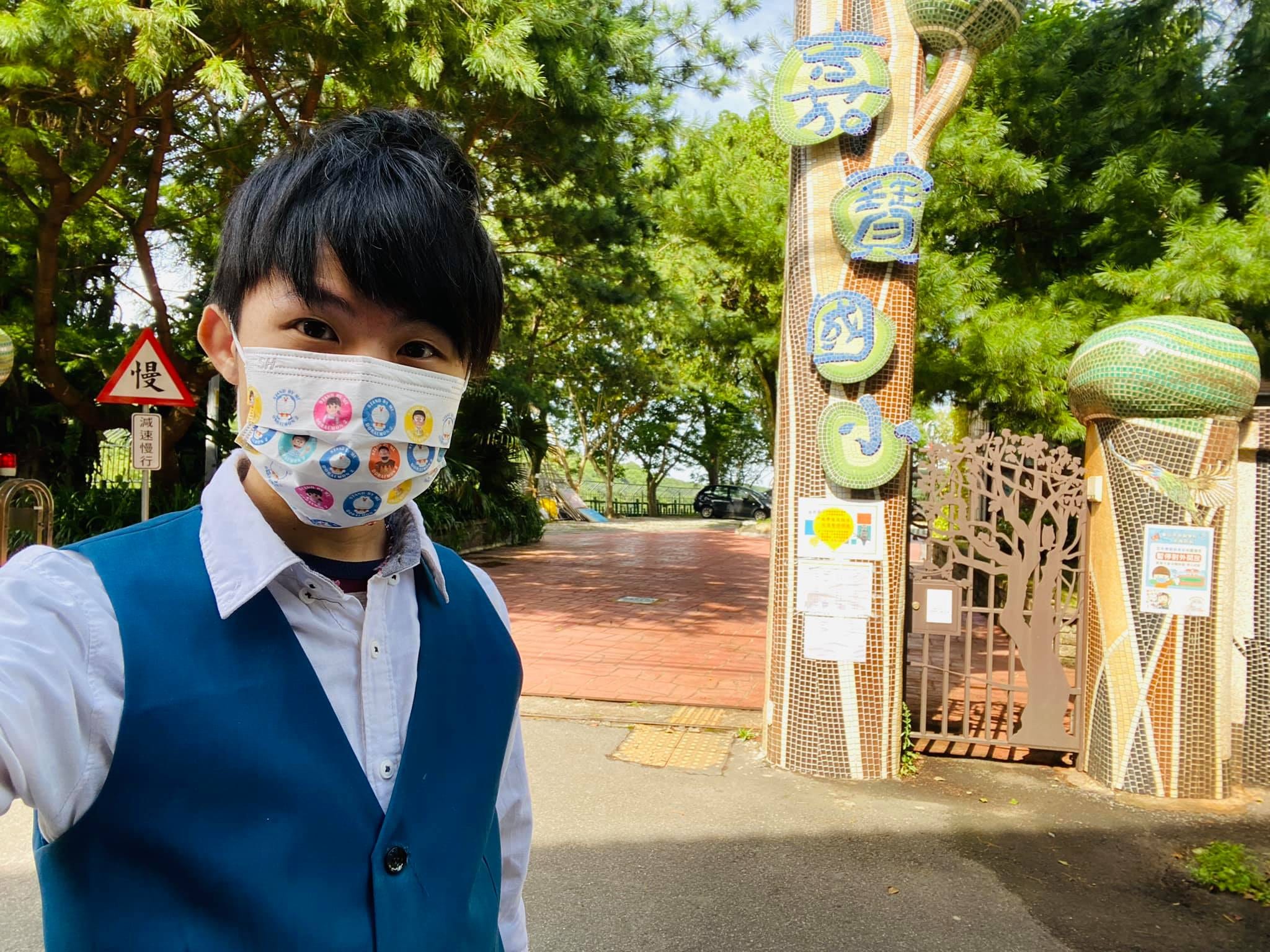 柯男戴著卡通口罩，在嘉寶國小馬賽克校門前自拍