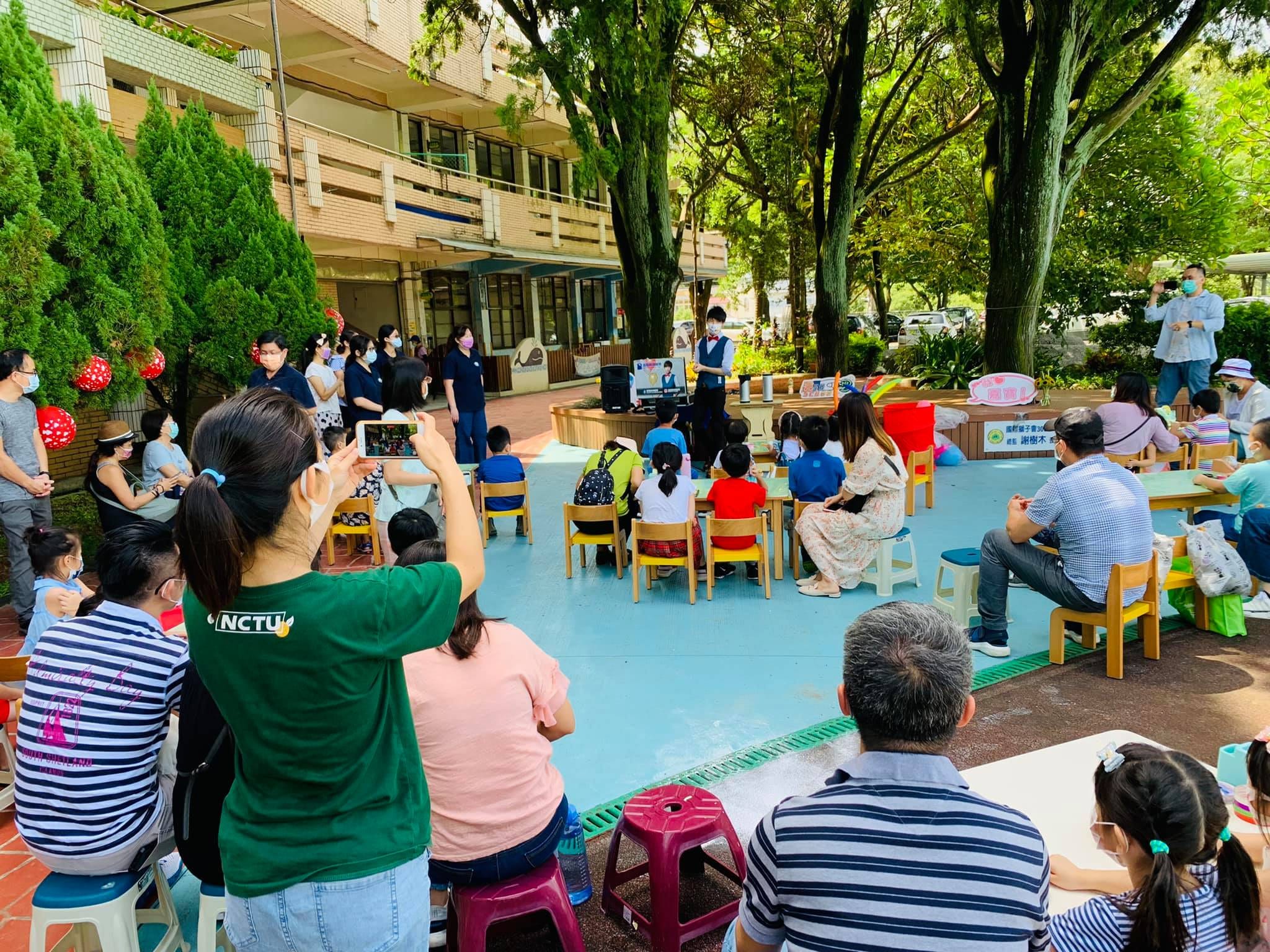 新北林口嘉寶國小中庭，親子觀眾圍坐看柯男在樹下舞台表演魔術