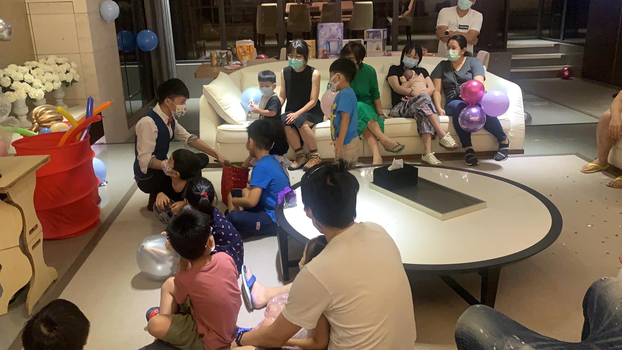 柯男蹲在客廳地上替小朋友折氣球,家長坐在沙發上觀看
