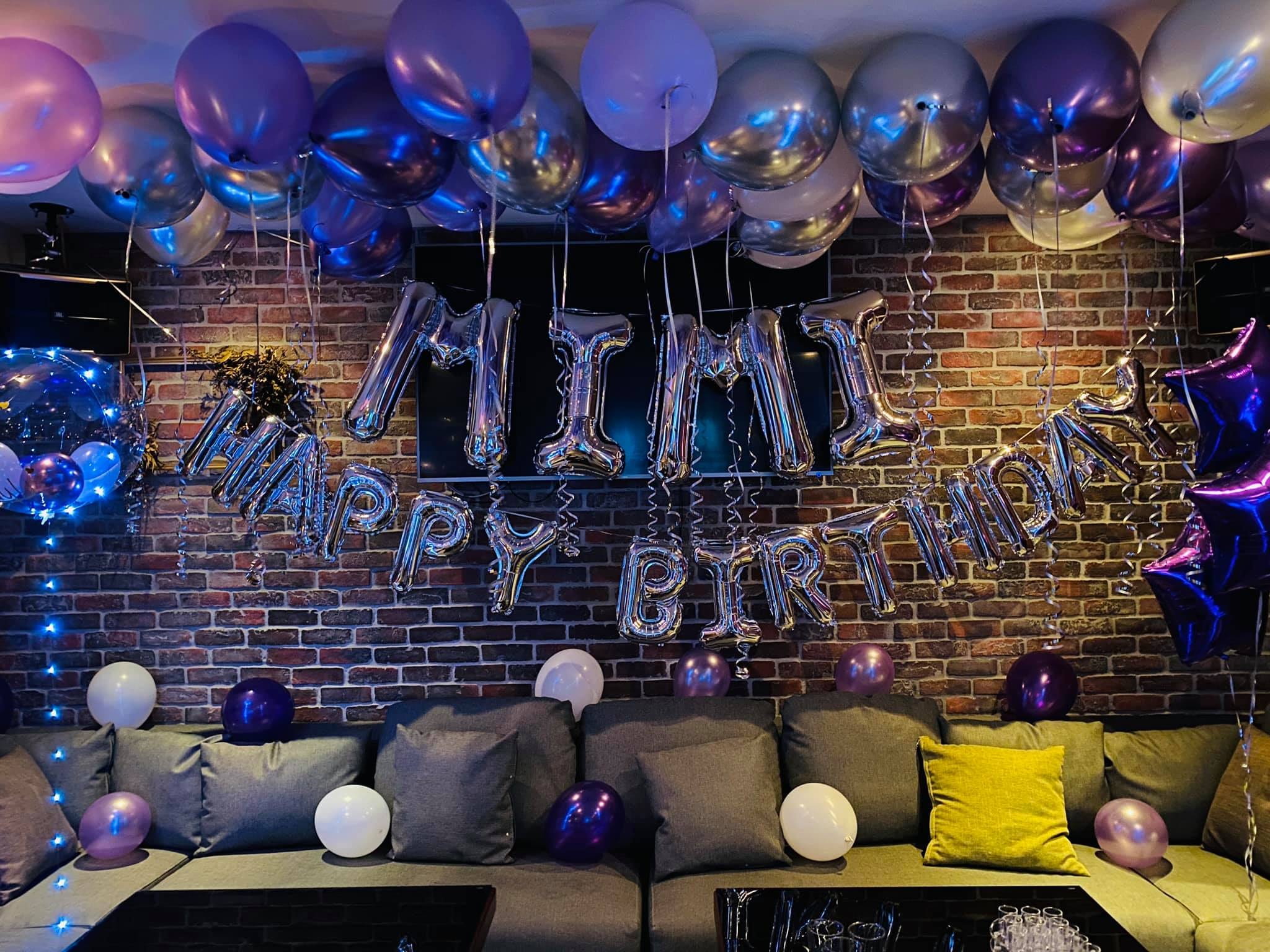 紅磚牆上的銀色名字與 HAPPY BIRTHDAY 字母氣球，上方紫銀空飄