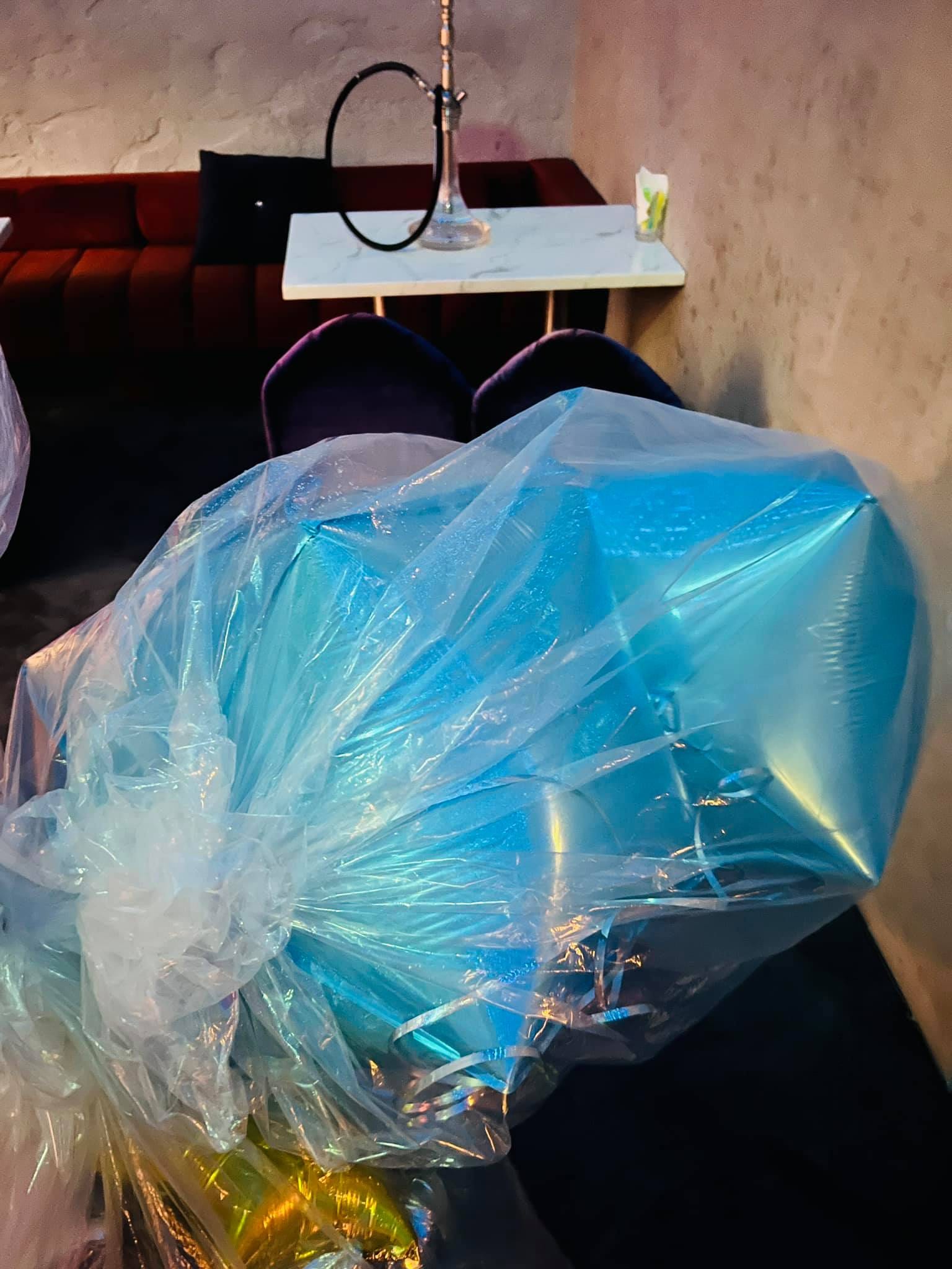 裝在大塑膠袋裡運送的藍色鋁箔與空飄氣球，放在酒吧座位旁