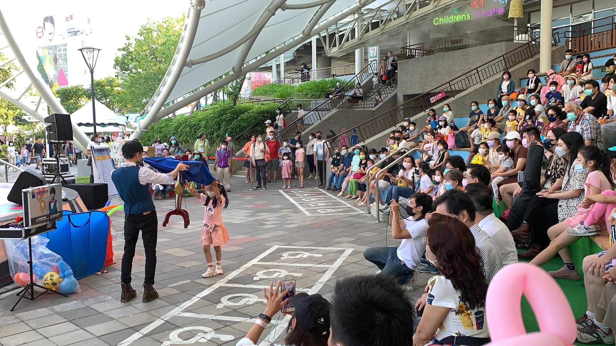 穿粉紅洋裝的小女孩上台,和柯男一起用藍色魔術布表演