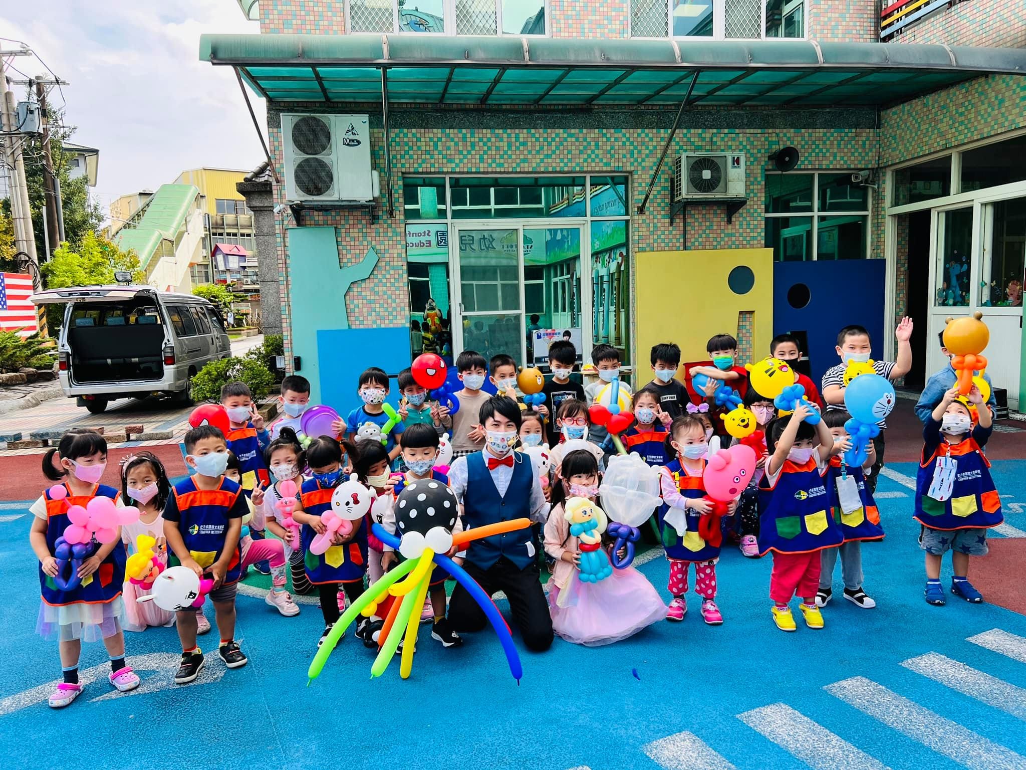 幼兒園操場上，穿園服的小朋友拿著造型氣球與柯男大合照