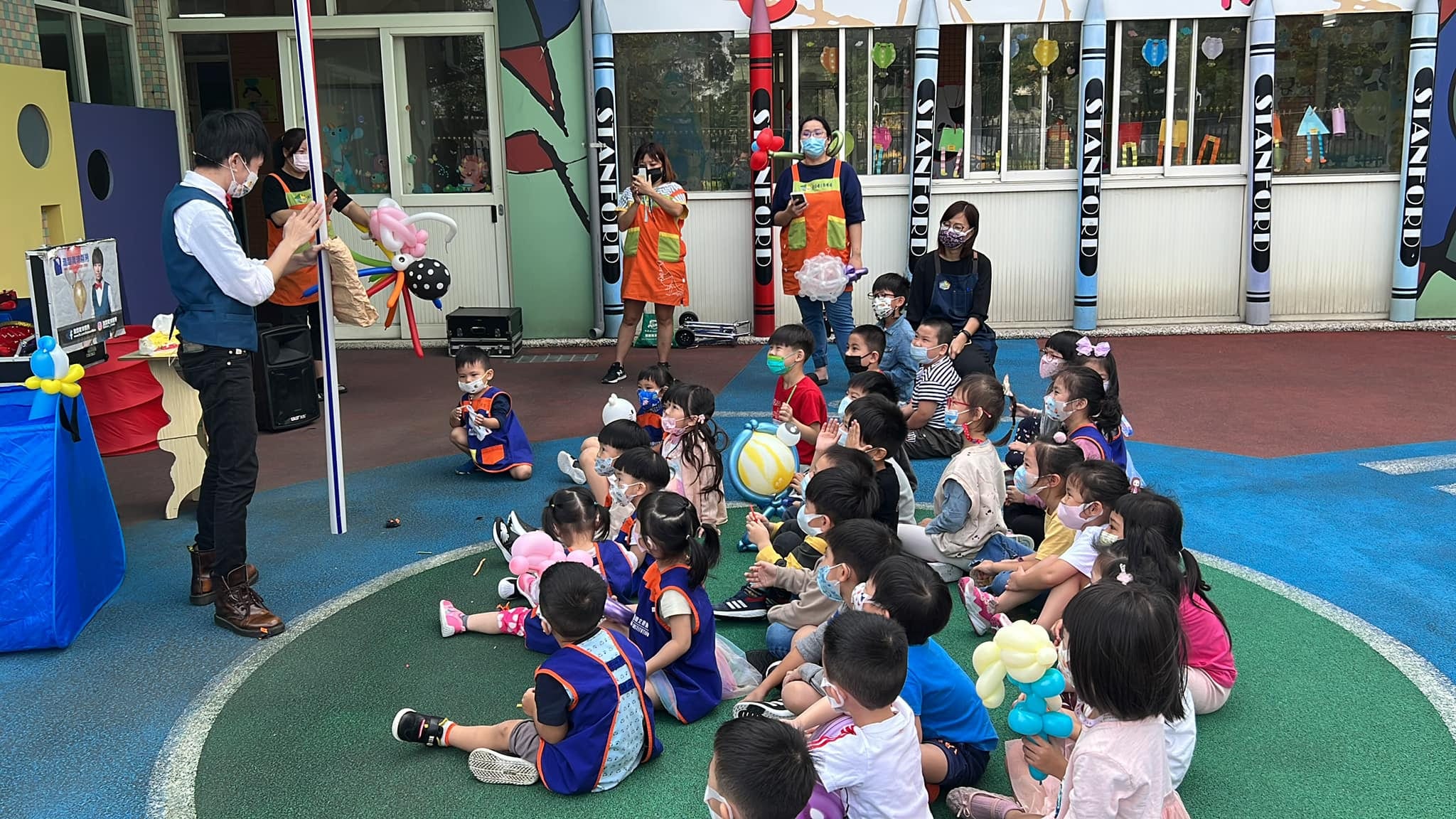 柯男在幼兒園操場表演魔術，小朋友坐在綠色地墊上觀看