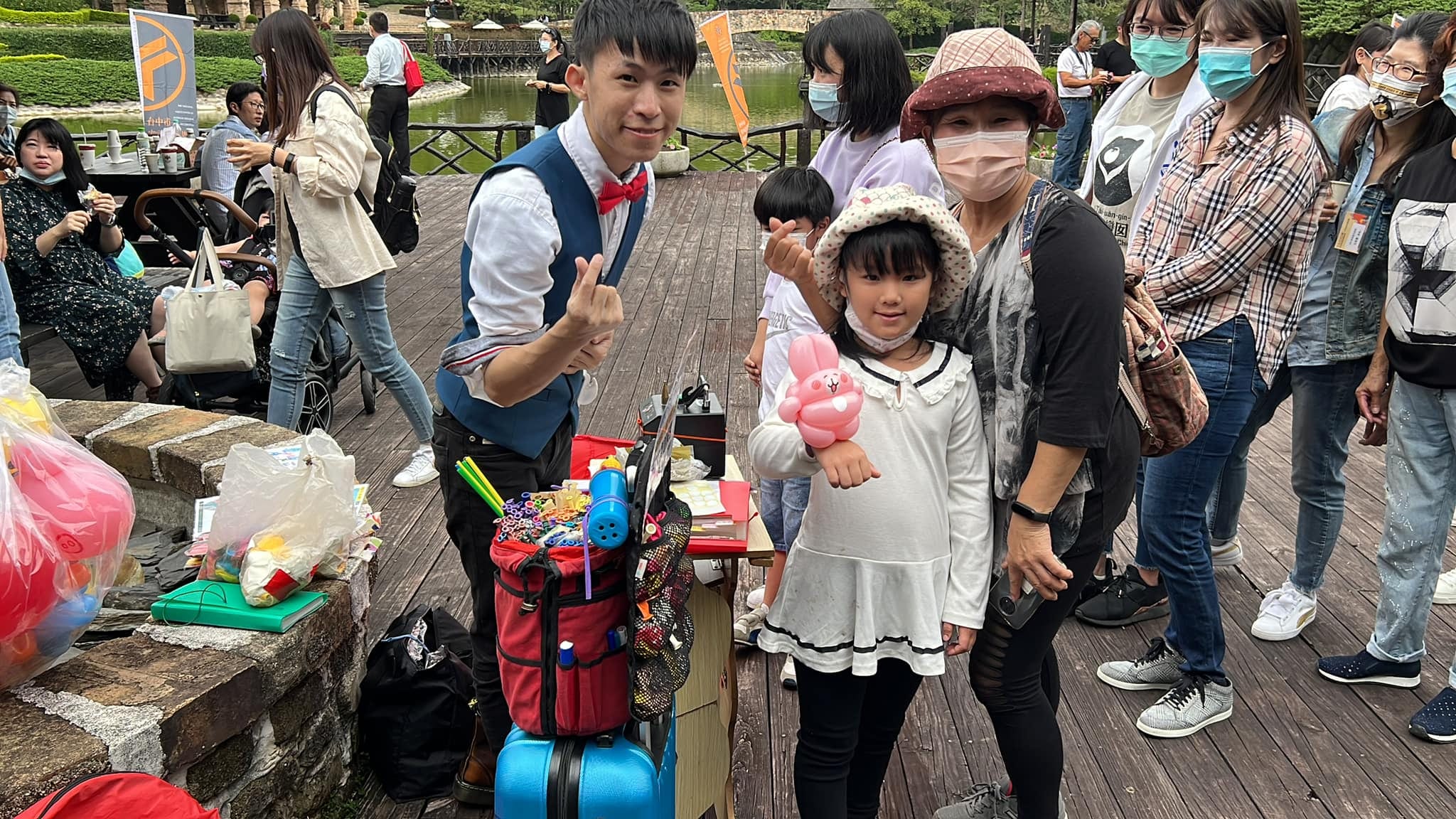 木棧道上的折氣球攤位，小女孩拿著粉紅兔子手環氣球