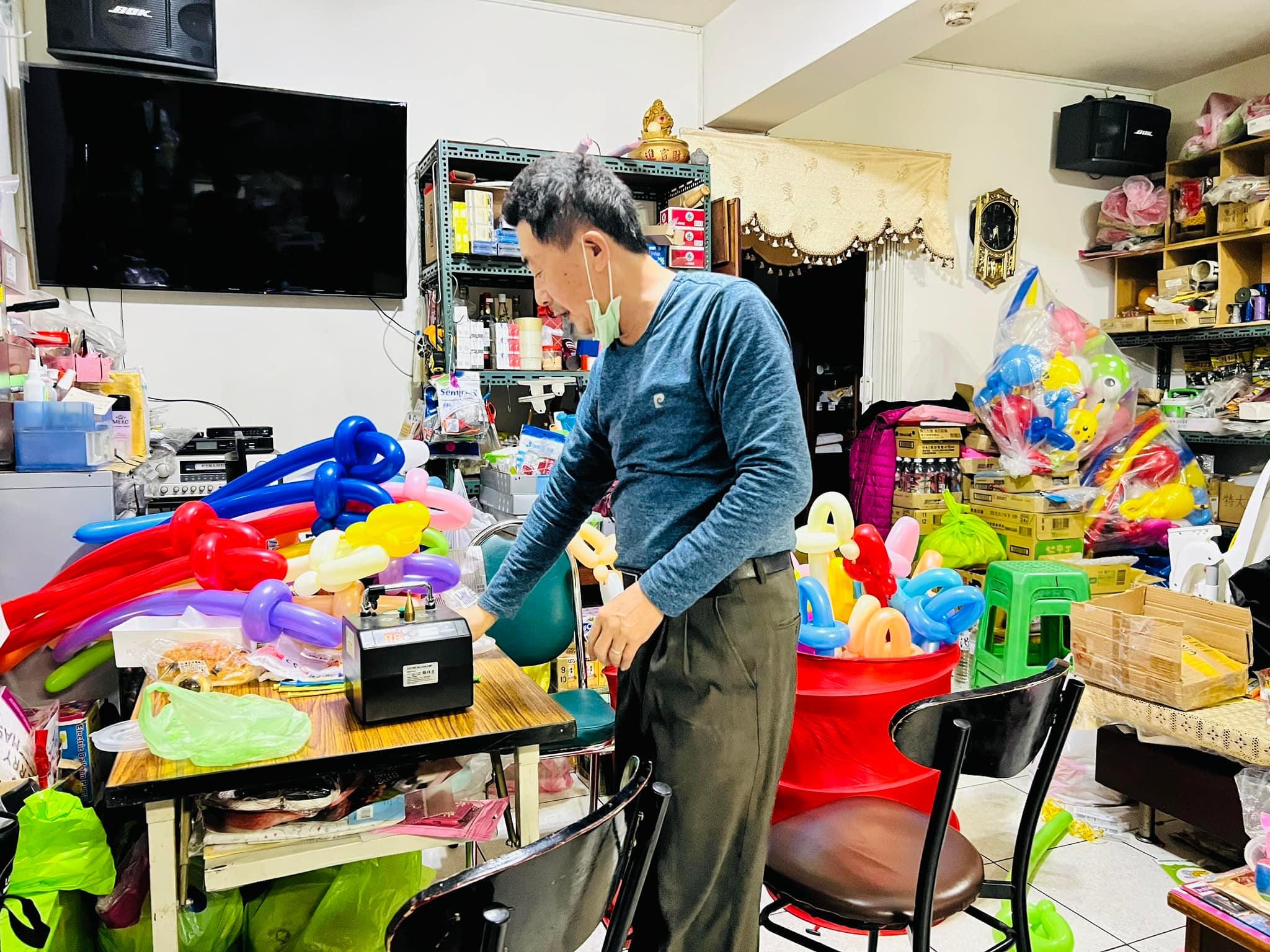 柯爹在家中工作室用打氣機做氣球寶劍，桌上堆滿彩色氣球