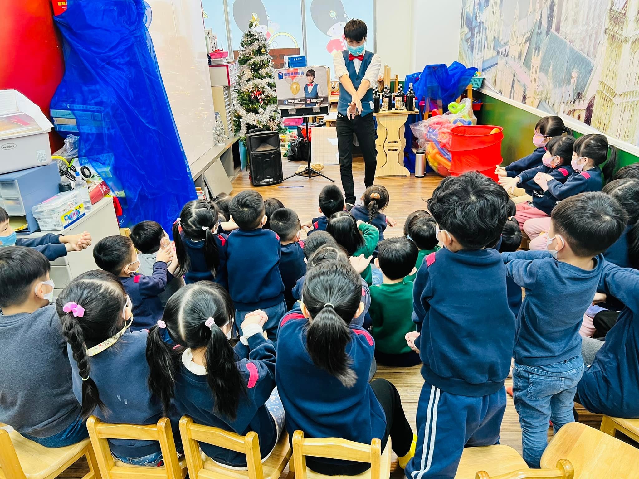 幼兒園教室裡,柯男在聖誕樹旁替小朋友表演魔術