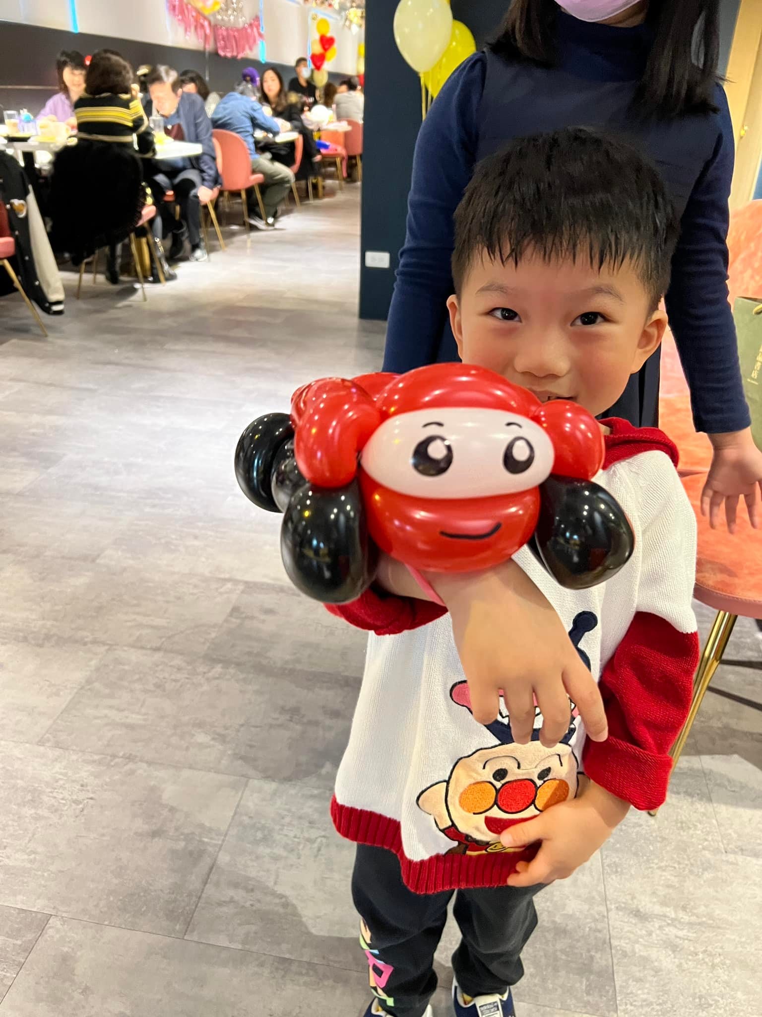 小男孩手上套著紅色小汽車造型氣球