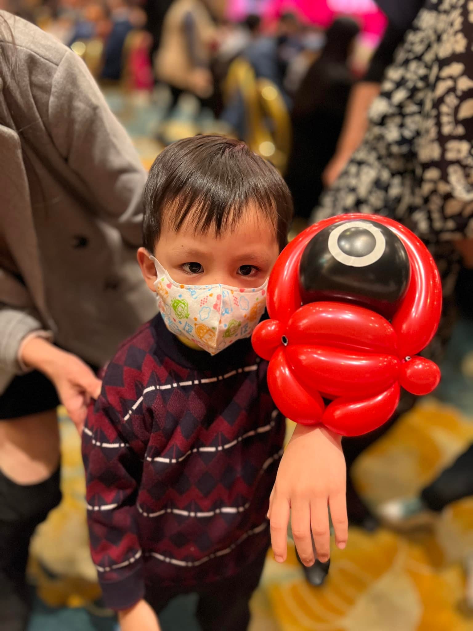 小男孩手上套著紅色魷魚遊戲面具人造型氣球