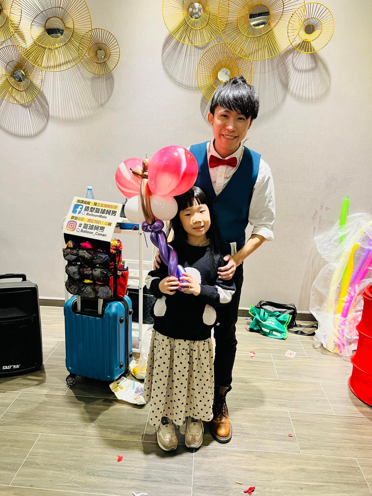 小女孩拿著粉紅愛心與紫色造型氣球，和柯男合照