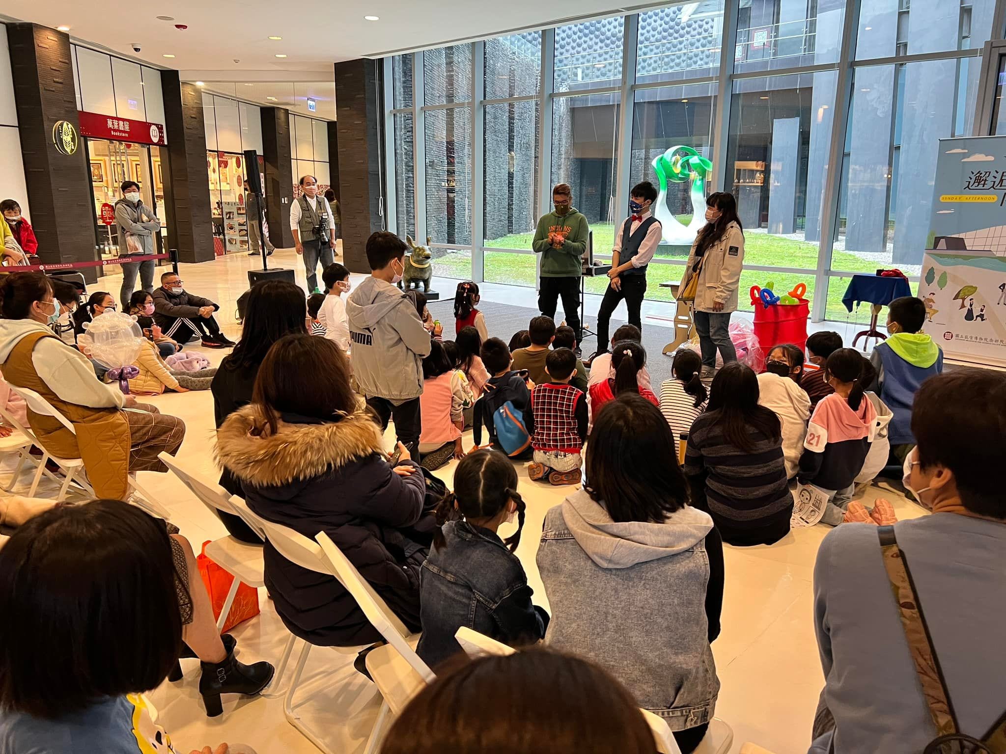 故宮南院大廳落地窗前，家長與小朋友坐著看表演