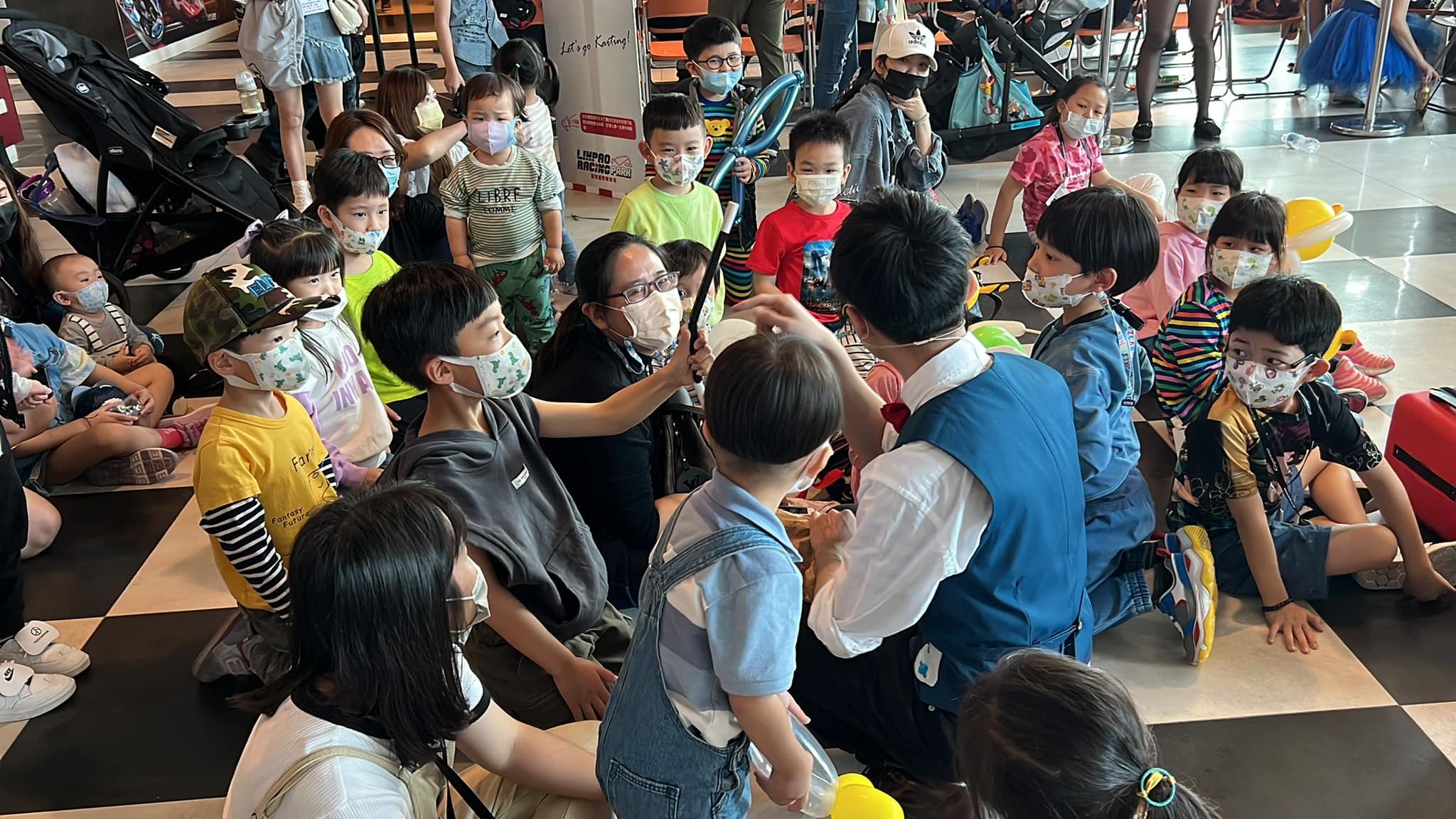 小朋友坐在黑白格地板上，等柯男現場折造型氣球