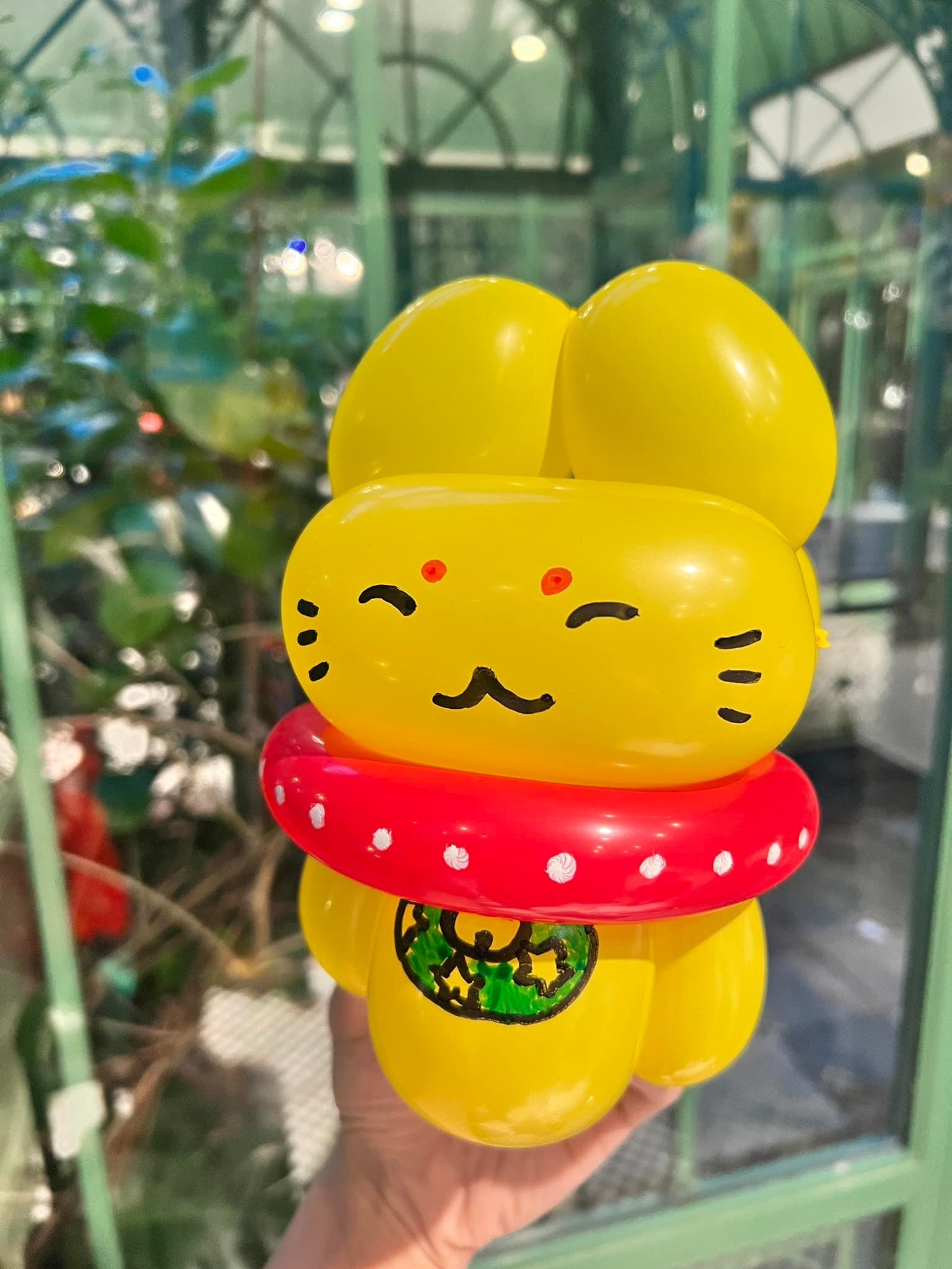 黃色招財貓造型氣球，瞇眼微笑，脖子上是白點紅色項圈，胸前掛著綠色金幣