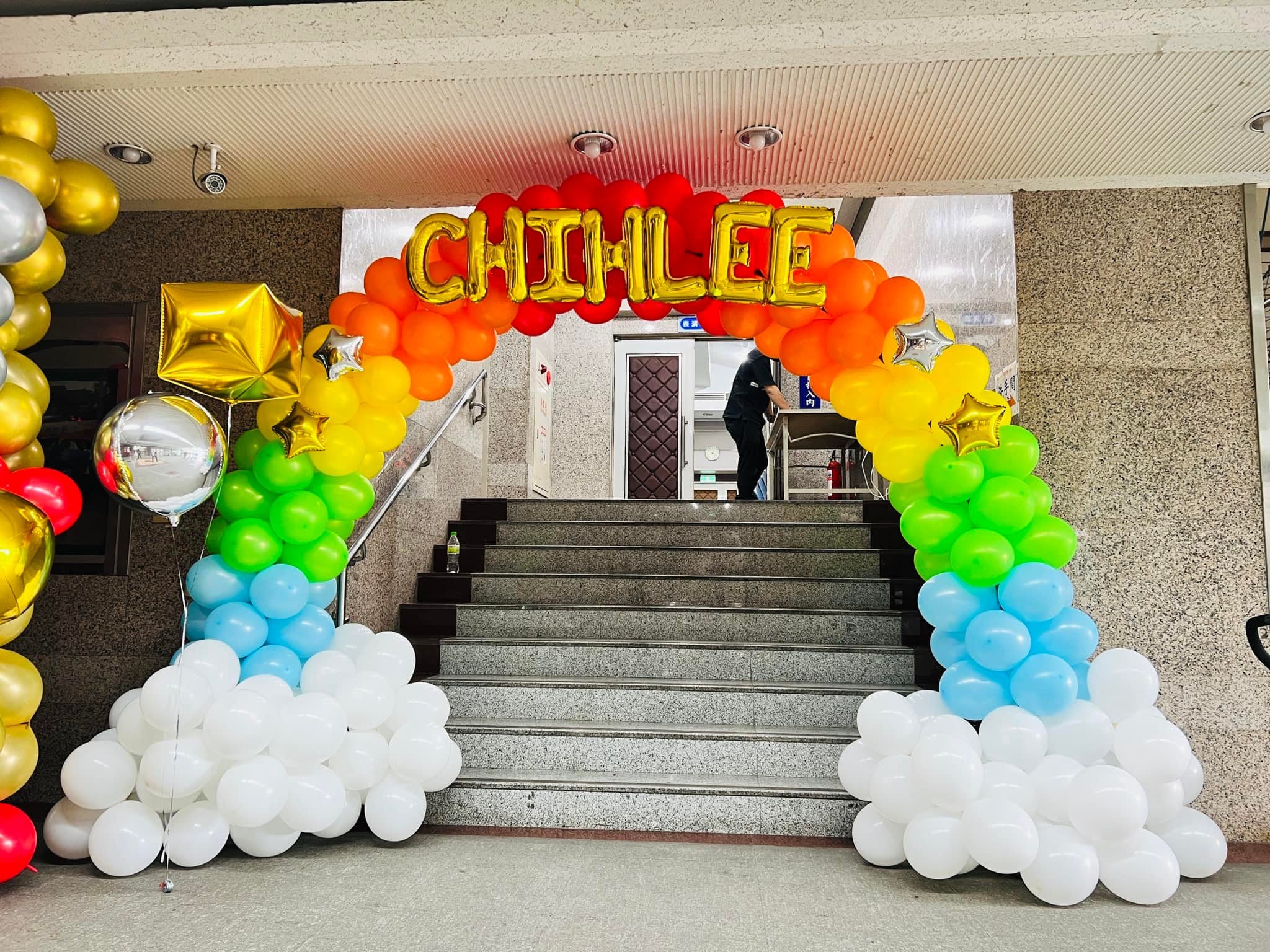 致理科大樓梯口的 CHIHLEE 彩虹氣球拱門,兩側是白色雲朵底座