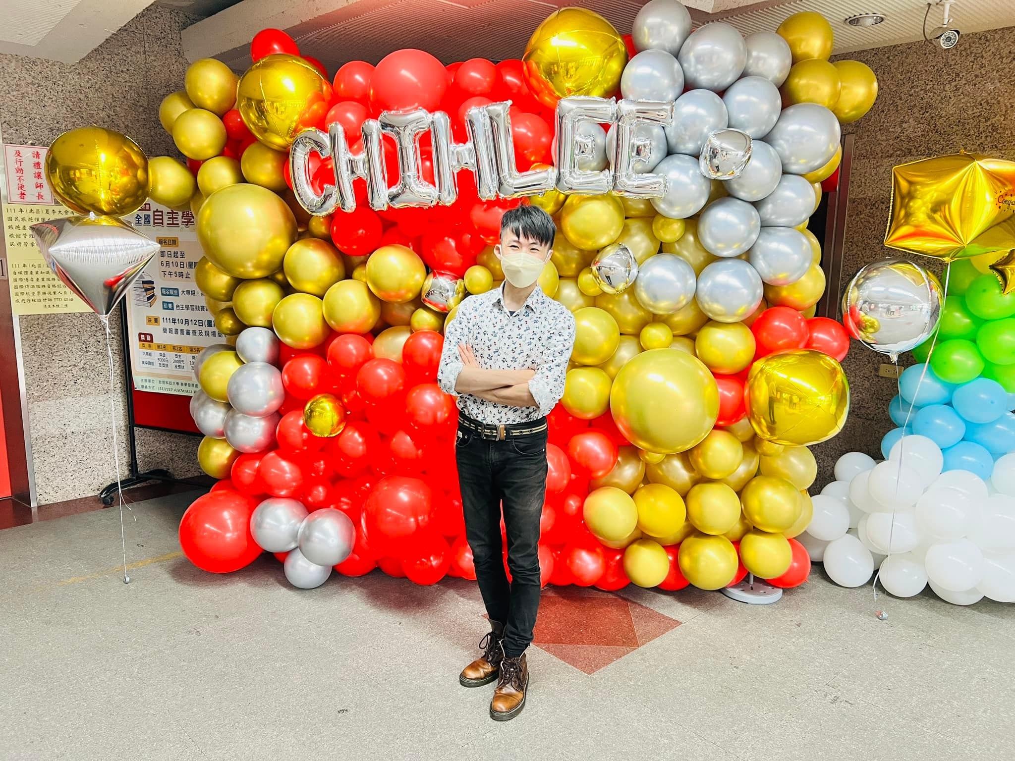 柯男站在紅金銀 CHIHLEE 字母氣球牆前,旁邊是彩虹與白雲氣球