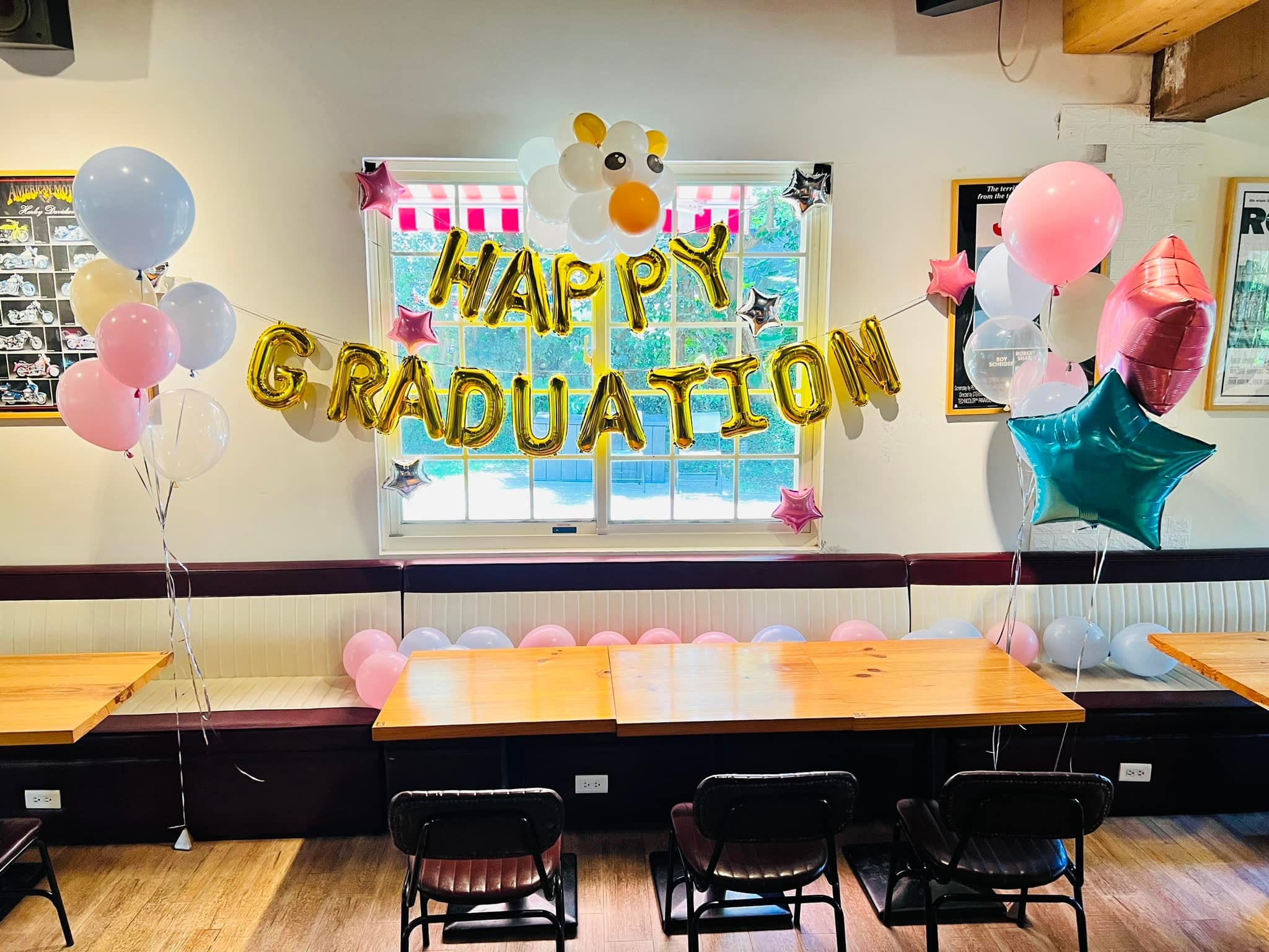 餐廳窗邊掛著金色 HAPPY GRADUATION 字母氣球與粉藍空飄氣球